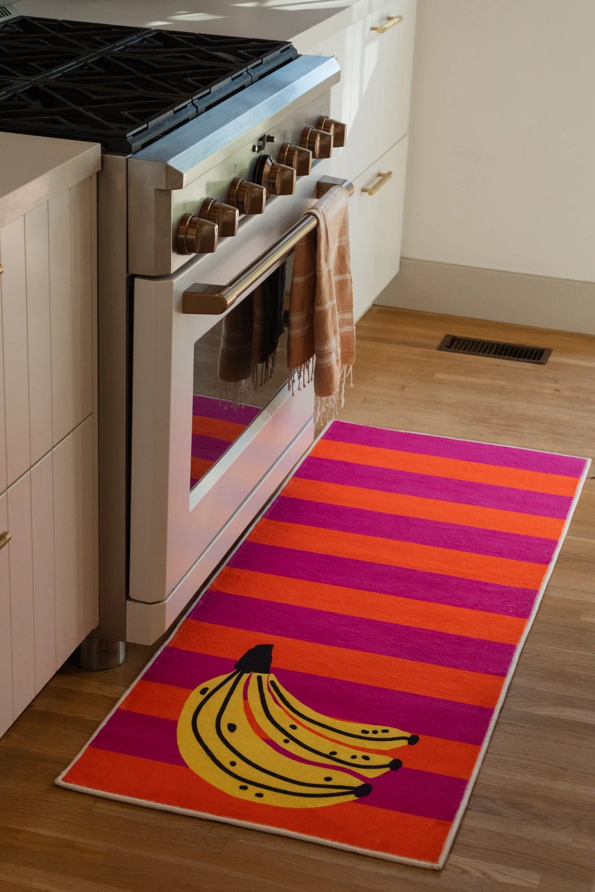 Colorful Striped Banana Fruit Runner Rug by Zoe Wodarz beside a white kitchen oven on a light wood floor