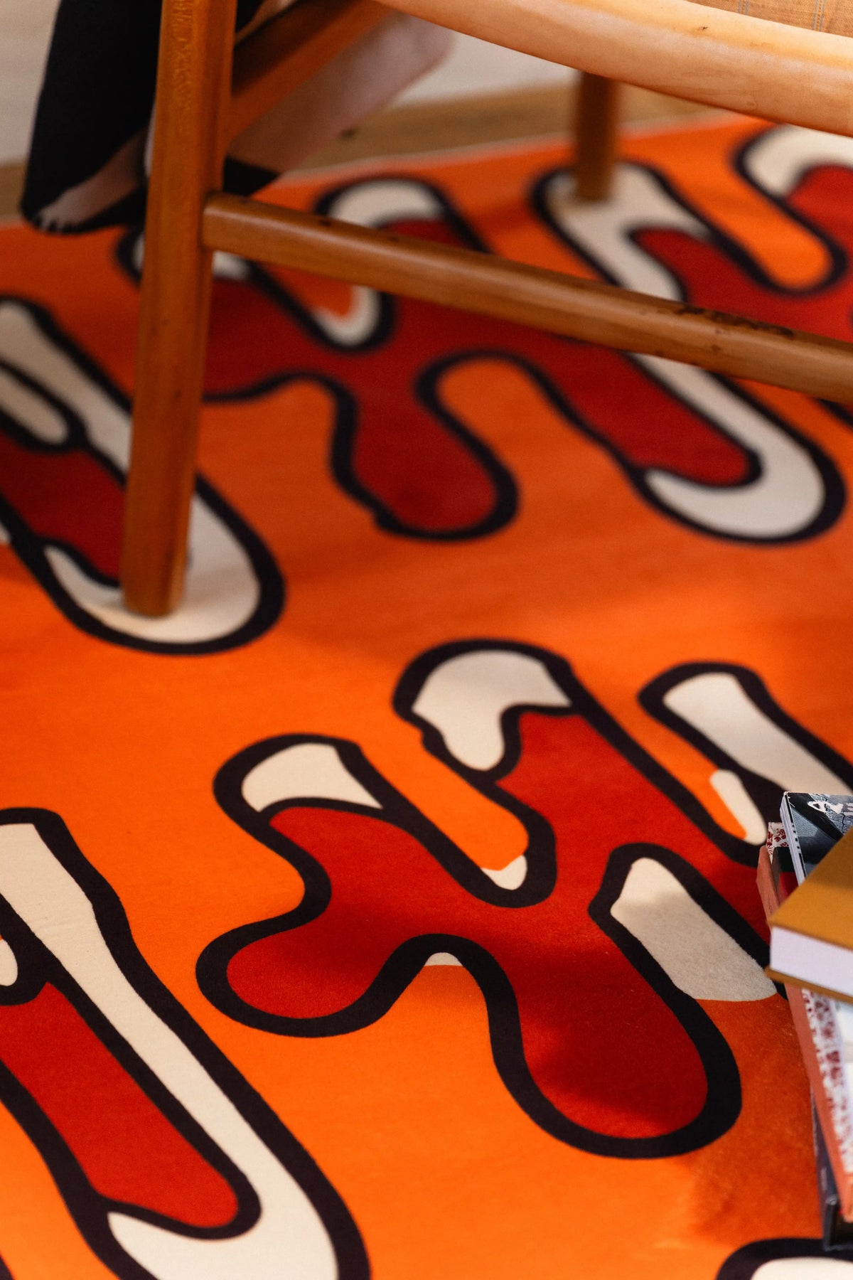 Red and cream squiggles outlined in black beneath wooden chair legs on an orange rug.