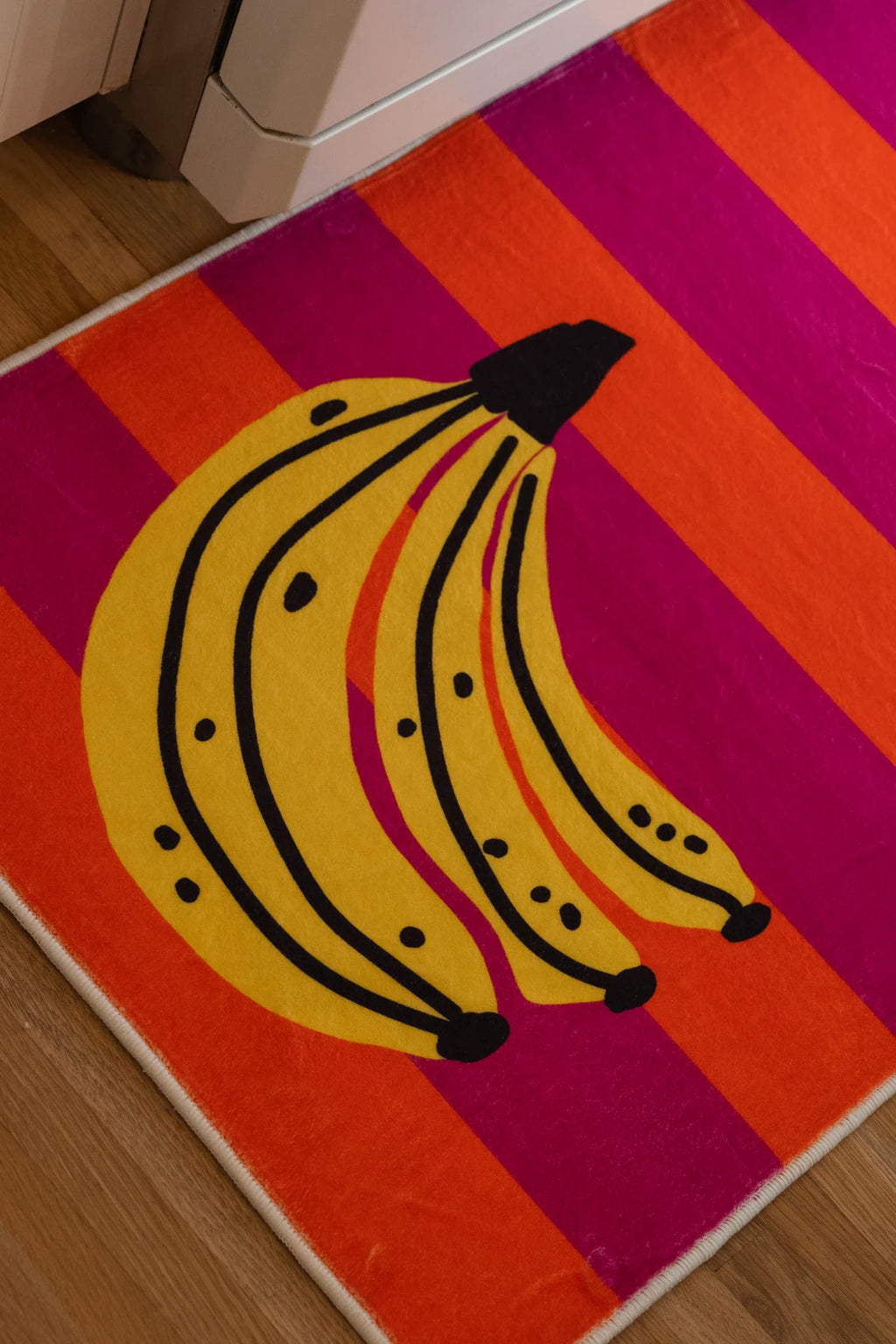 Corner detail of the banana runner rug showing the fruit motif, white edge, and saturated striped pattern