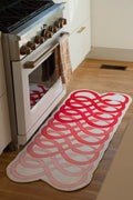 Red abstract loop snake runner rug beside a white kitchen oven on a light wood floor, with interlocking loop forms