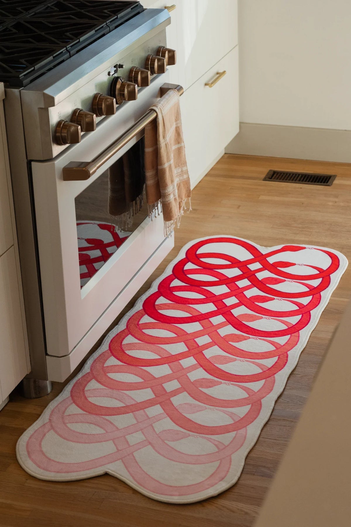 Red abstract loop snake runner rug beside a white kitchen oven on a light wood floor, with interlocking loop forms