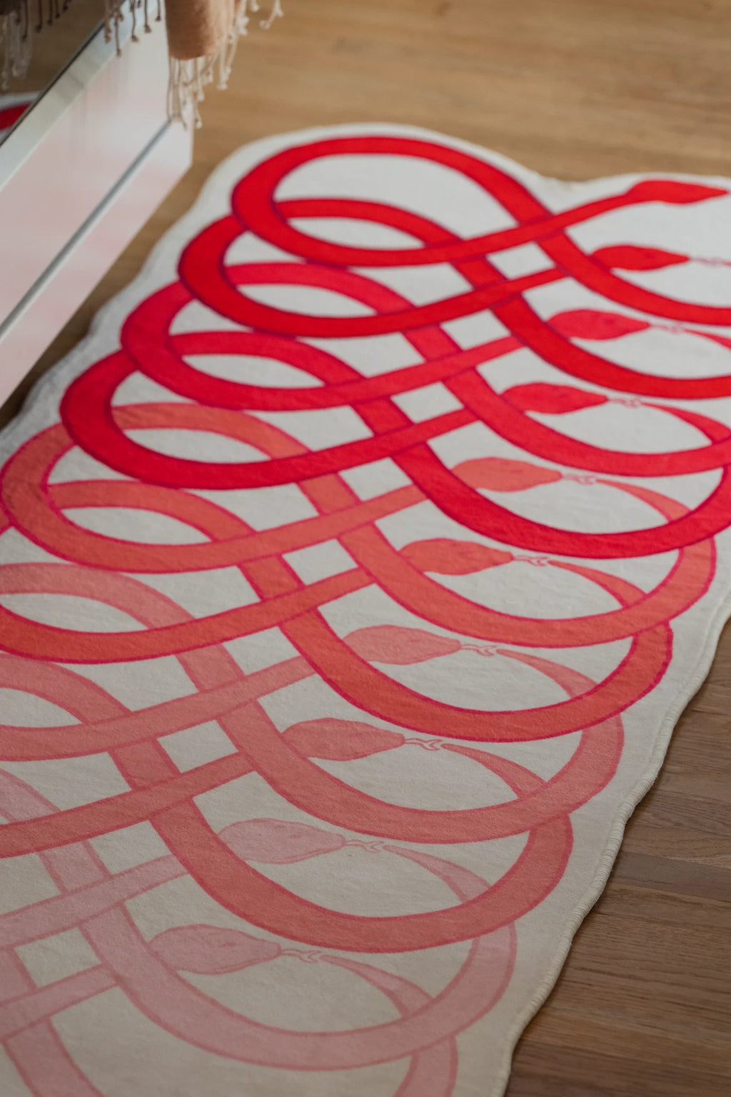 Abstract loop runner rug in front of white cabinetry, with overlapping red bands creating a flowing snake pattern