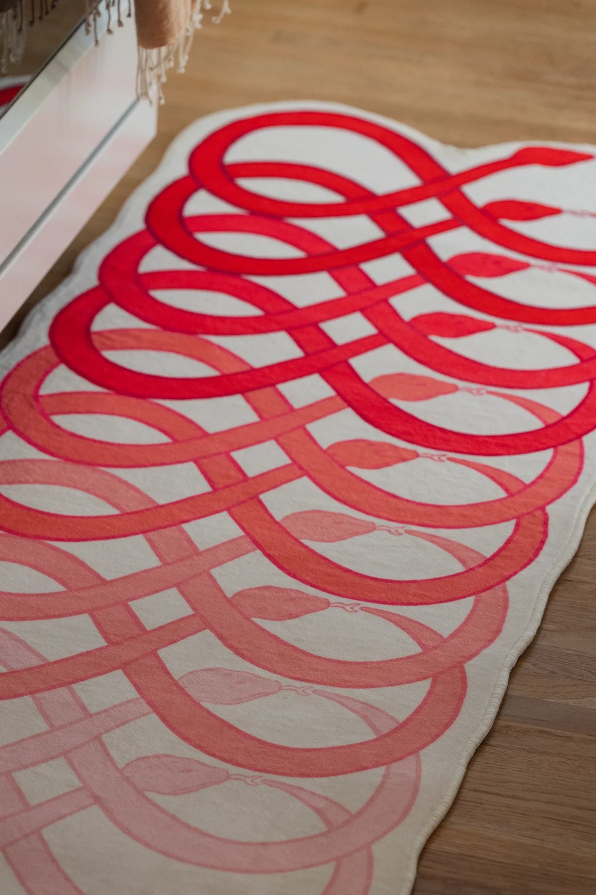Abstract loop runner rug in front of white cabinetry, with overlapping red bands creating a flowing snake pattern