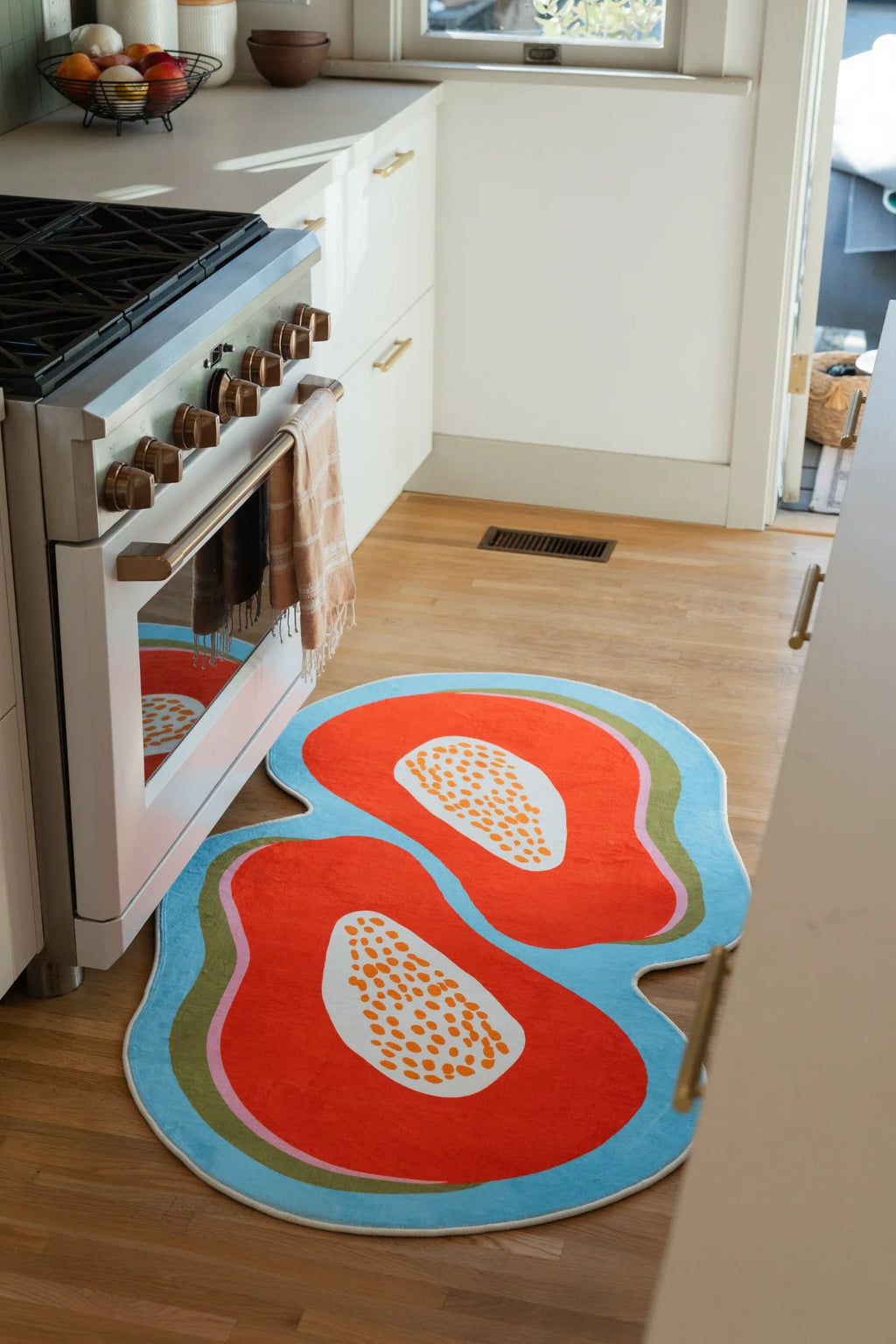 Papaya fruit rug beside a white oven and cabinets, showing the blue outline and irregular rounded shape