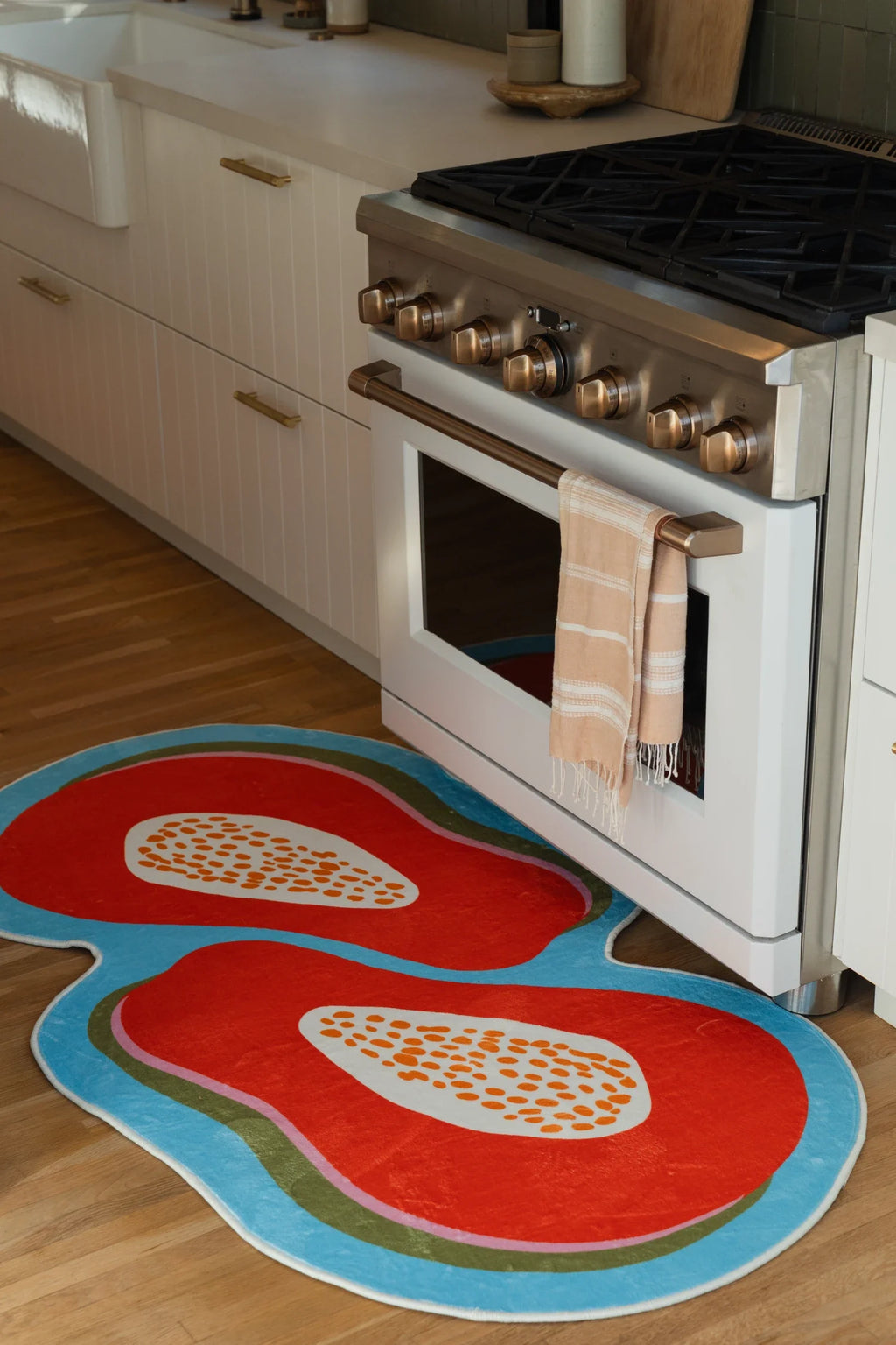 Orange papaya rug in front of a white kitchen range, showing two sliced fruit motifs on a wood floor