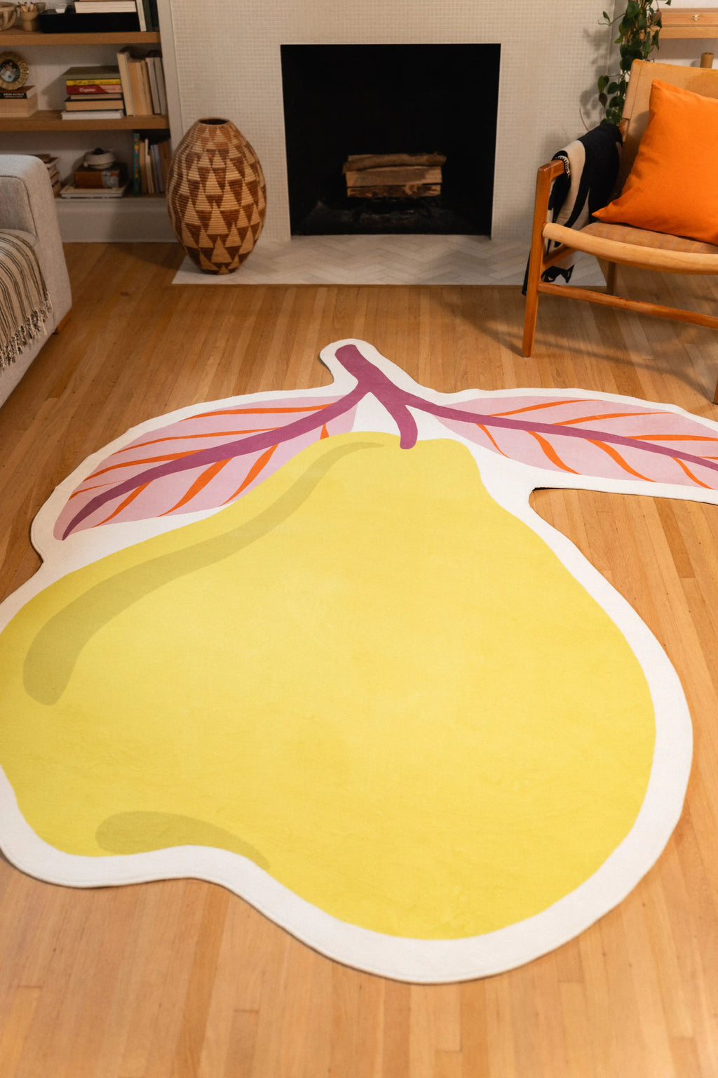 Large yellow pear body with a white border and pink leaves on a wood floor between a fireplace and wooden chair.