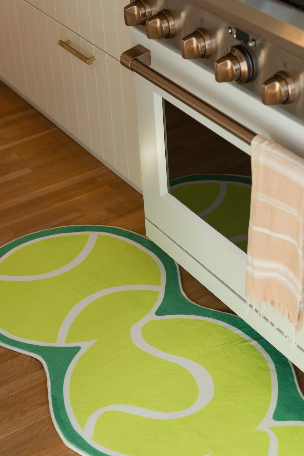 Partial view of the tennis inspired runner in front of a white oven, with layered green shapes on a wood floor