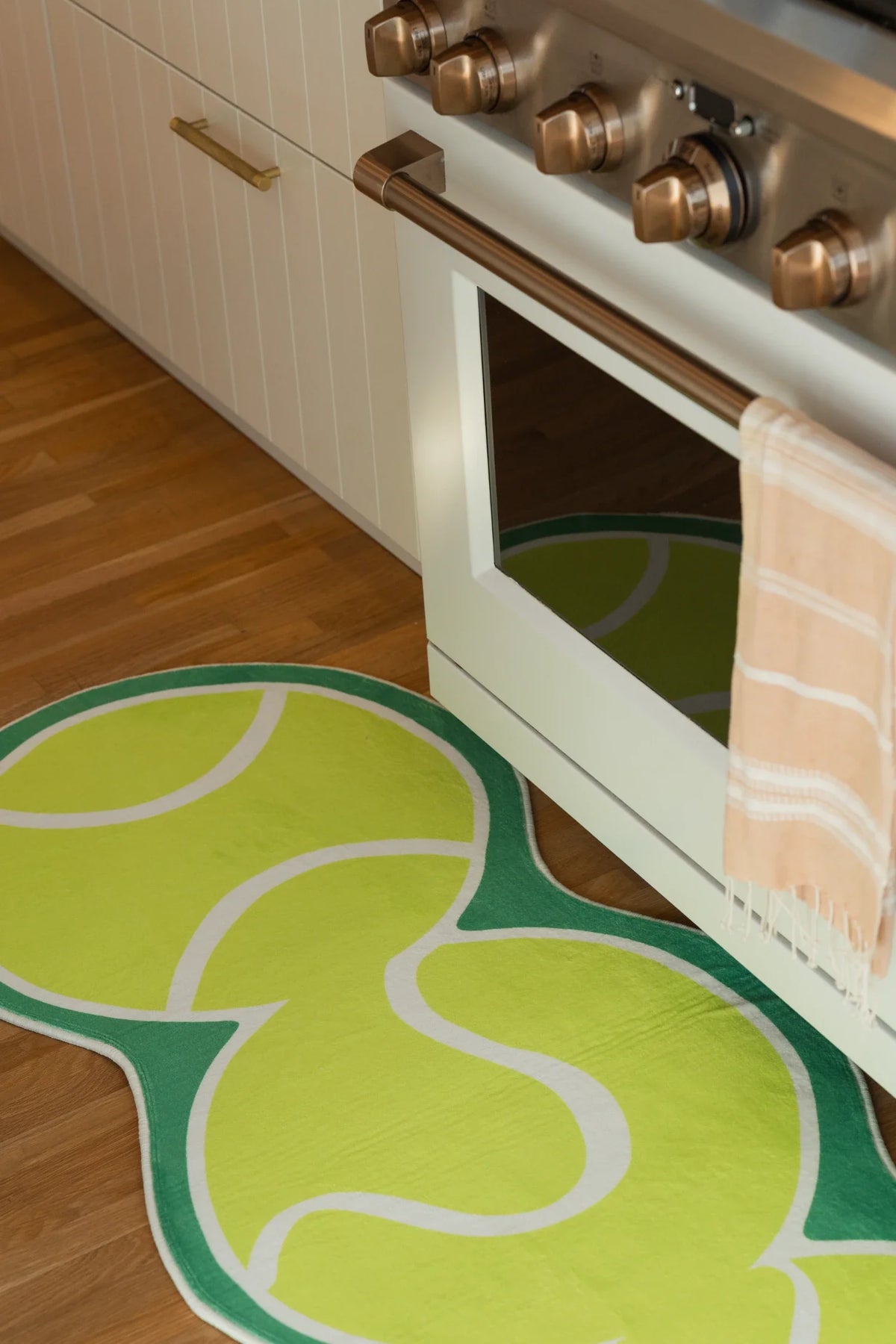 Partial view of the tennis inspired runner in front of a white oven, with layered green shapes on a wood floor