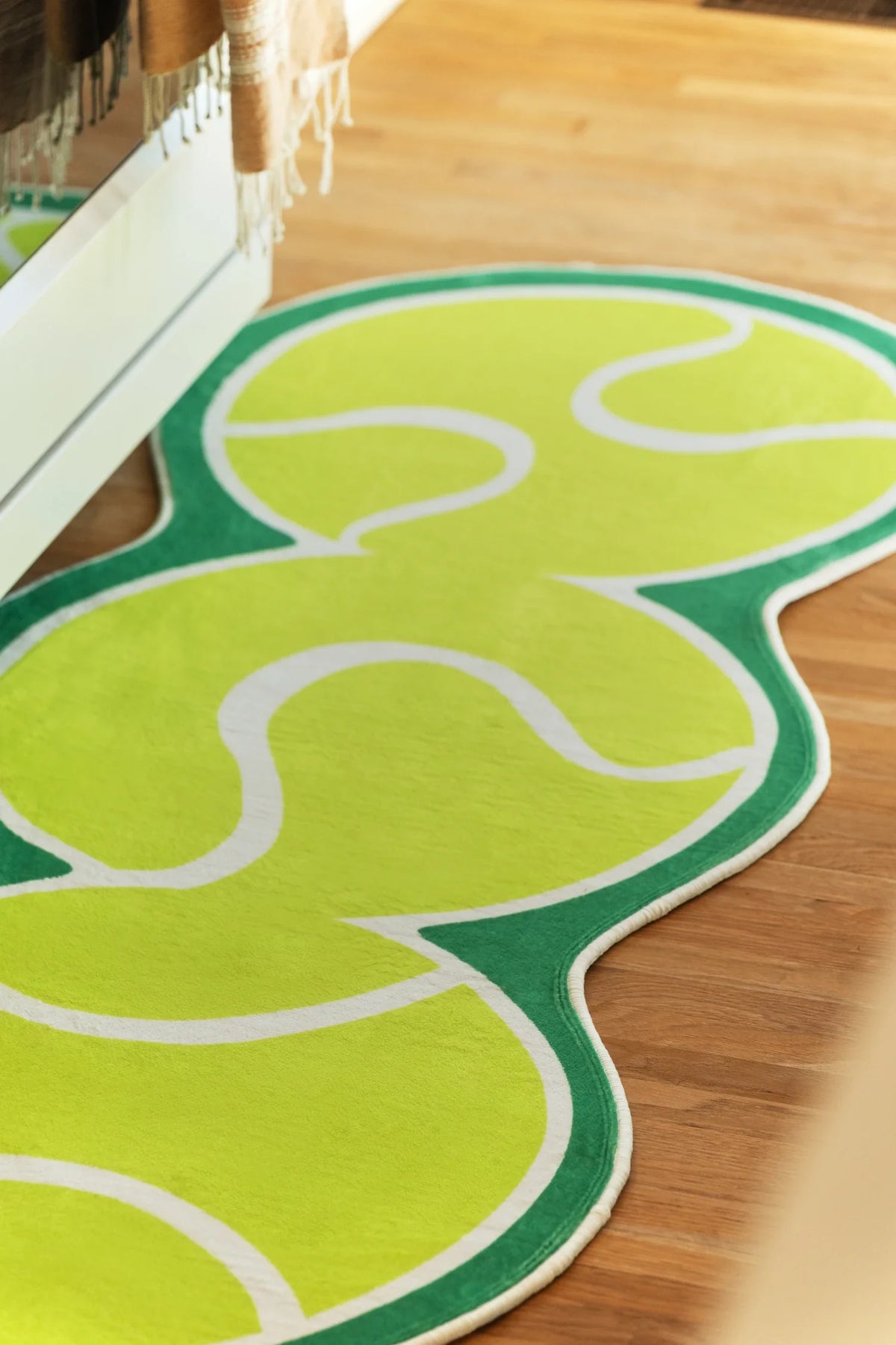 Irregular green runner rug in a bright kitchen walkway with sunlight across the surface and white cabinetry