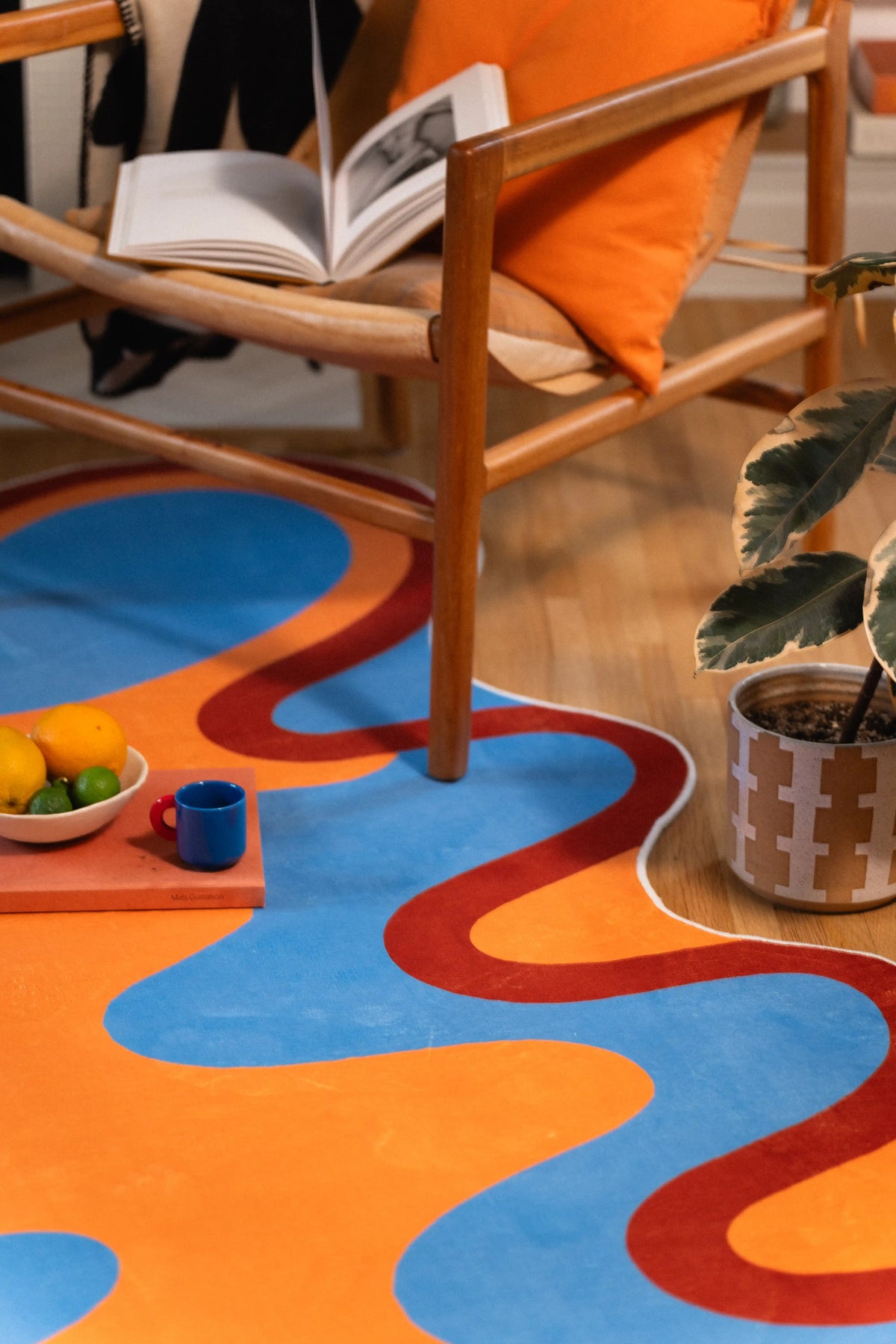 Wooden chair legs stand within the rust-edged curves, with an open book above and fruit tray beside them.