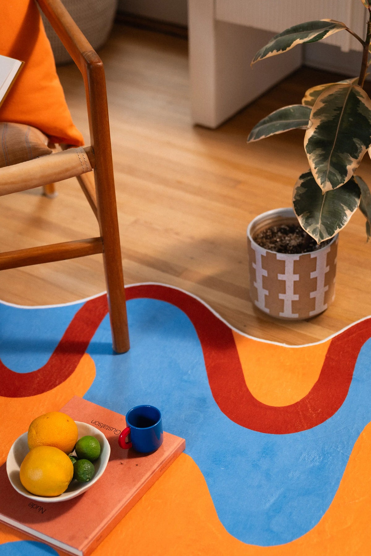 The rug’s uneven edge bends around a chair leg and patterned planter, with lemons placed on the orange section.