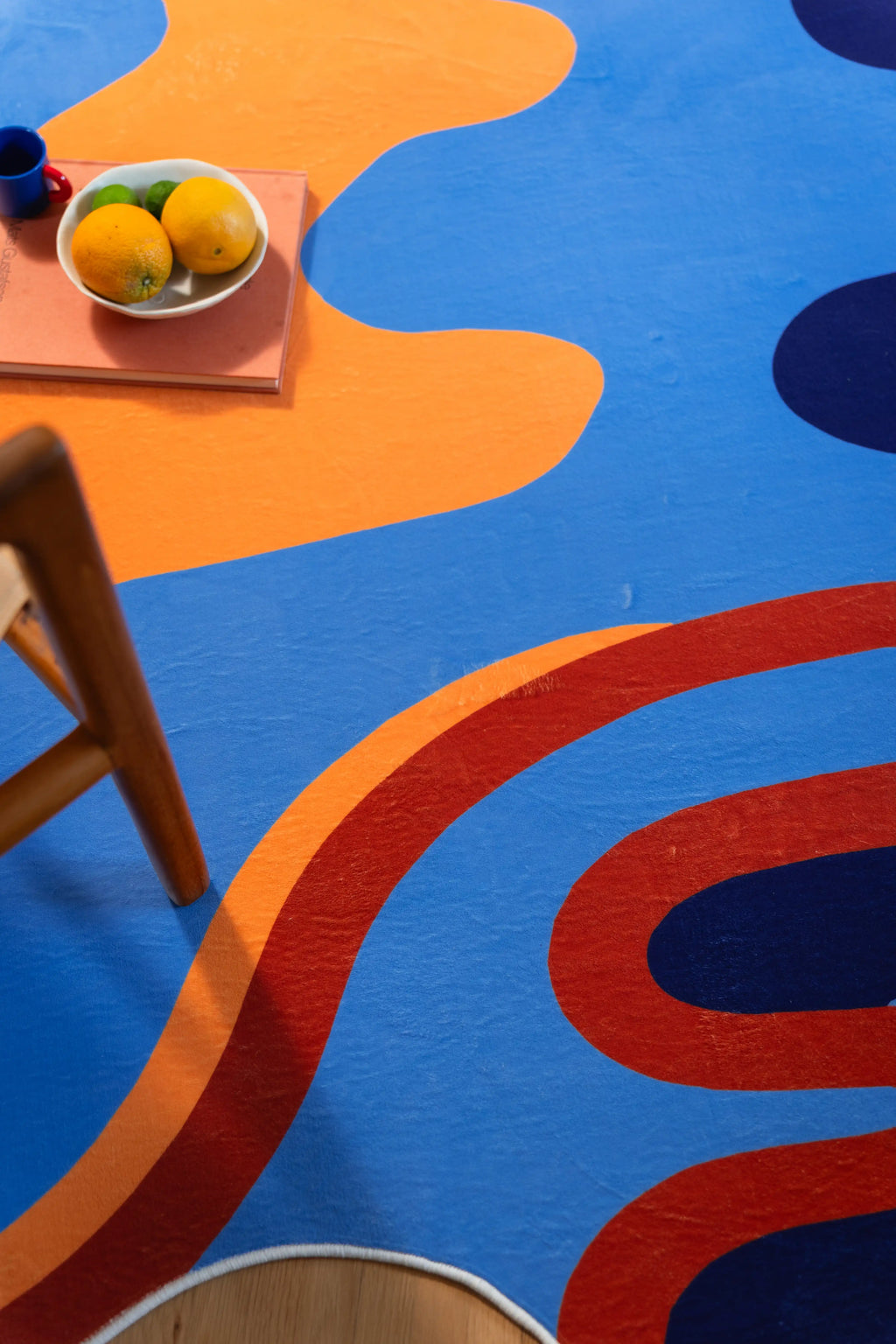 A sweeping rust line separates orange, sky blue, and navy in a top-down crop with a fruit bowl at the corner.