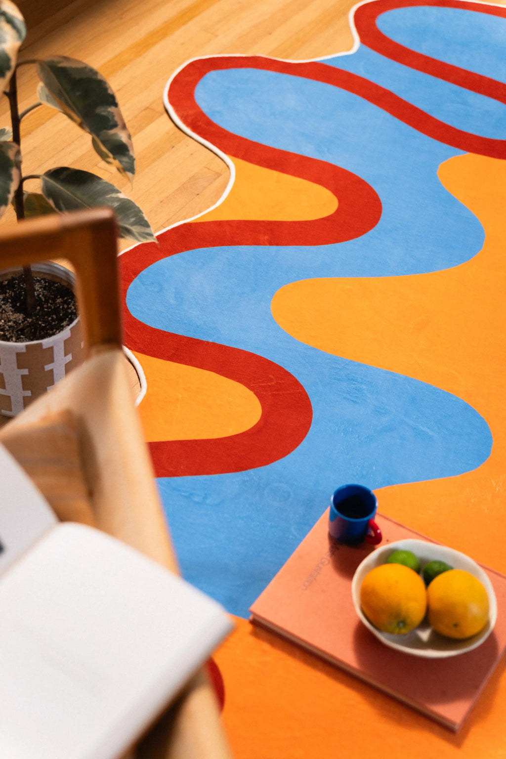 An open book frames the lower corner as rust outlines weave between sky-blue and orange sections of the rug.