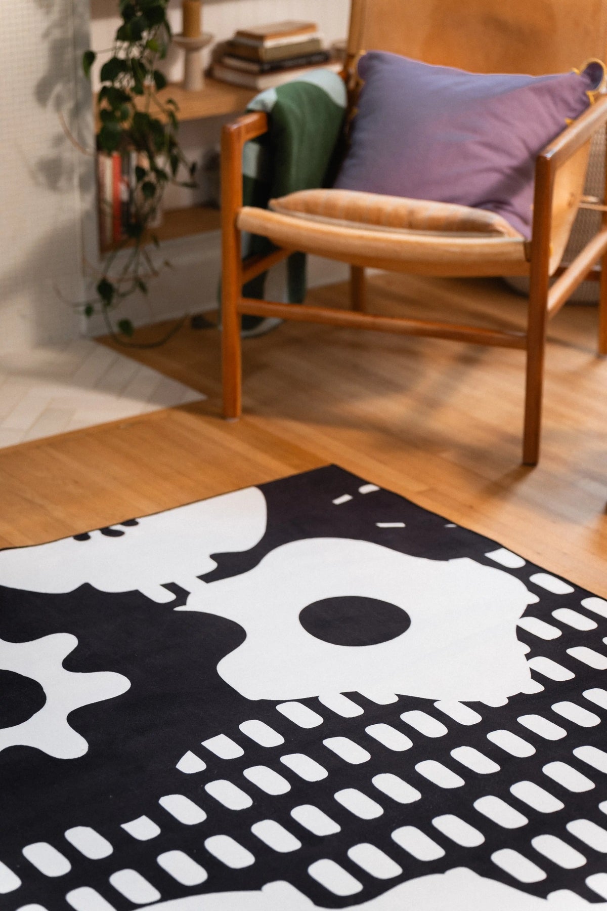Large white flower and black grid pattern on a rug beside a wooden chair with a purple cushion.
