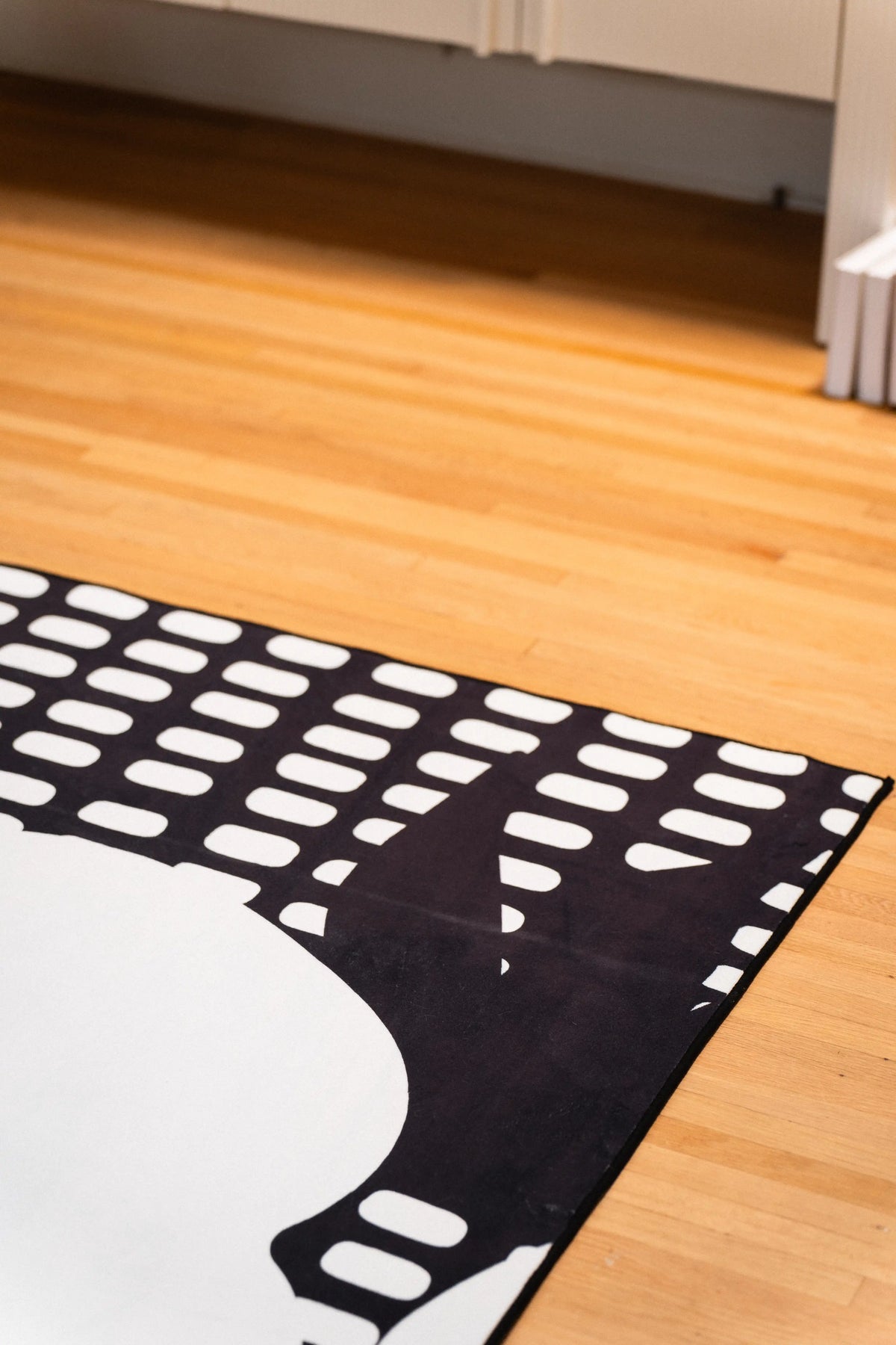 Rows of white rectangular marks and part of a white flower along a black rug edge beside a white cabinet.