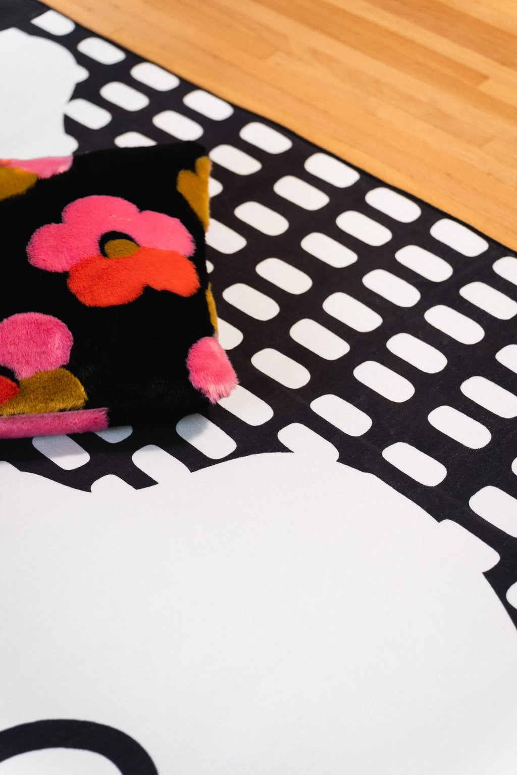 Colorful floral pillow on a black and white rug beside a large white flower and rectangular grid pattern.