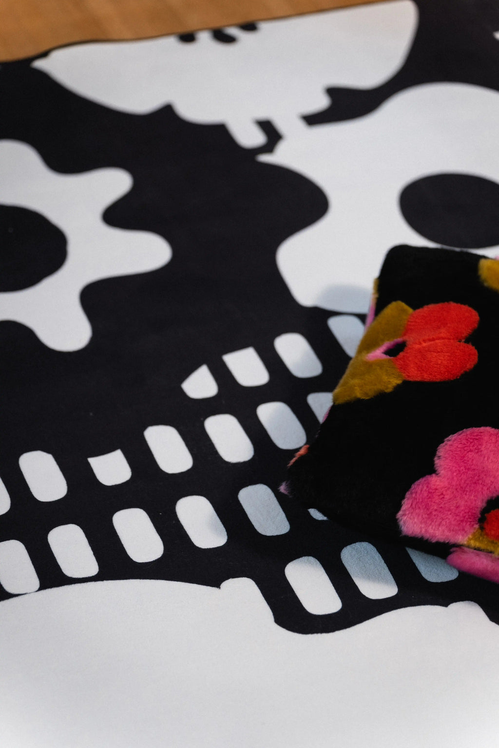 Black floral pillow beside white abstract flower shapes and rows of rectangular marks on a black rug.