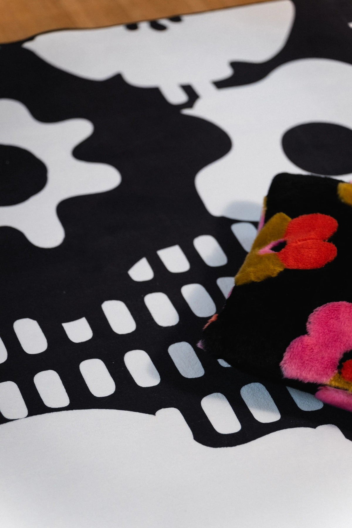 Black floral pillow beside white abstract flower shapes and rows of rectangular marks on a black rug.
