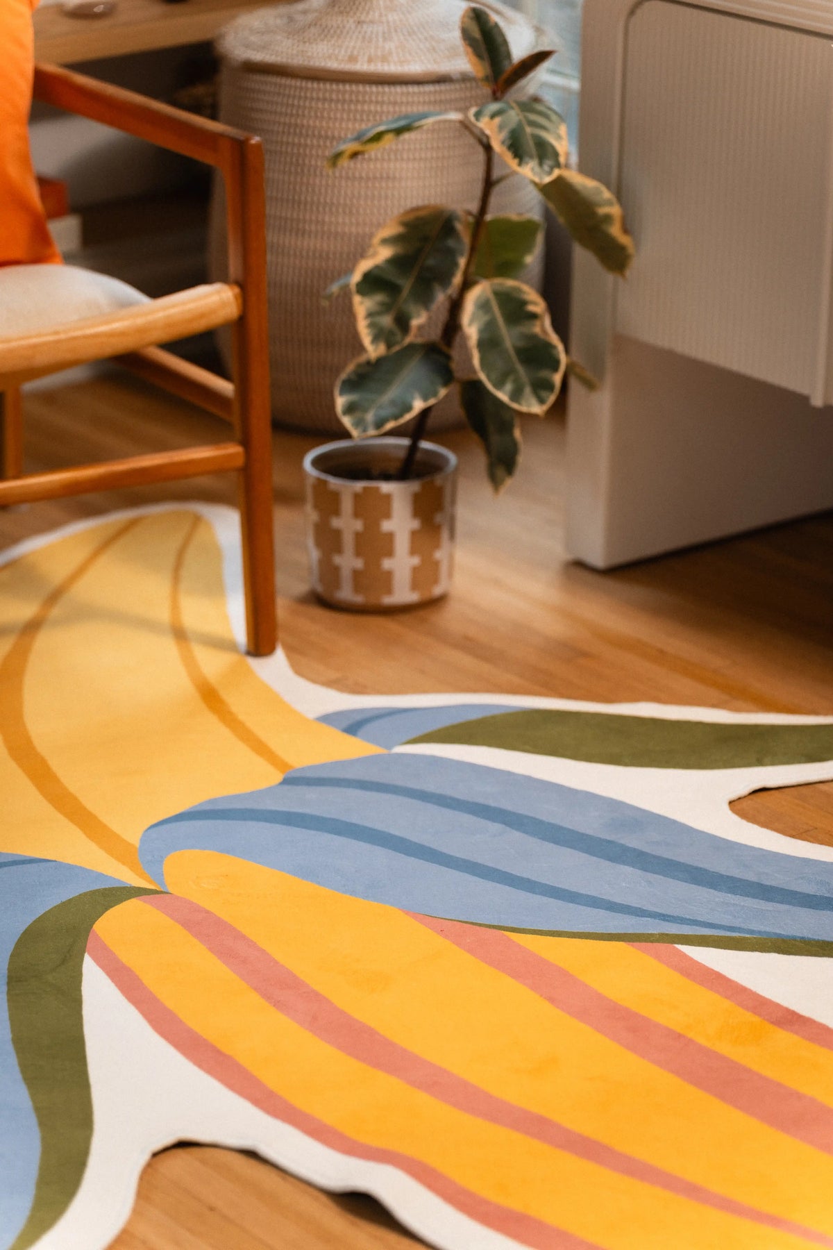 Blue and green banana peel sections crossing the yellow fruit beside a potted plant and wooden chair legs.