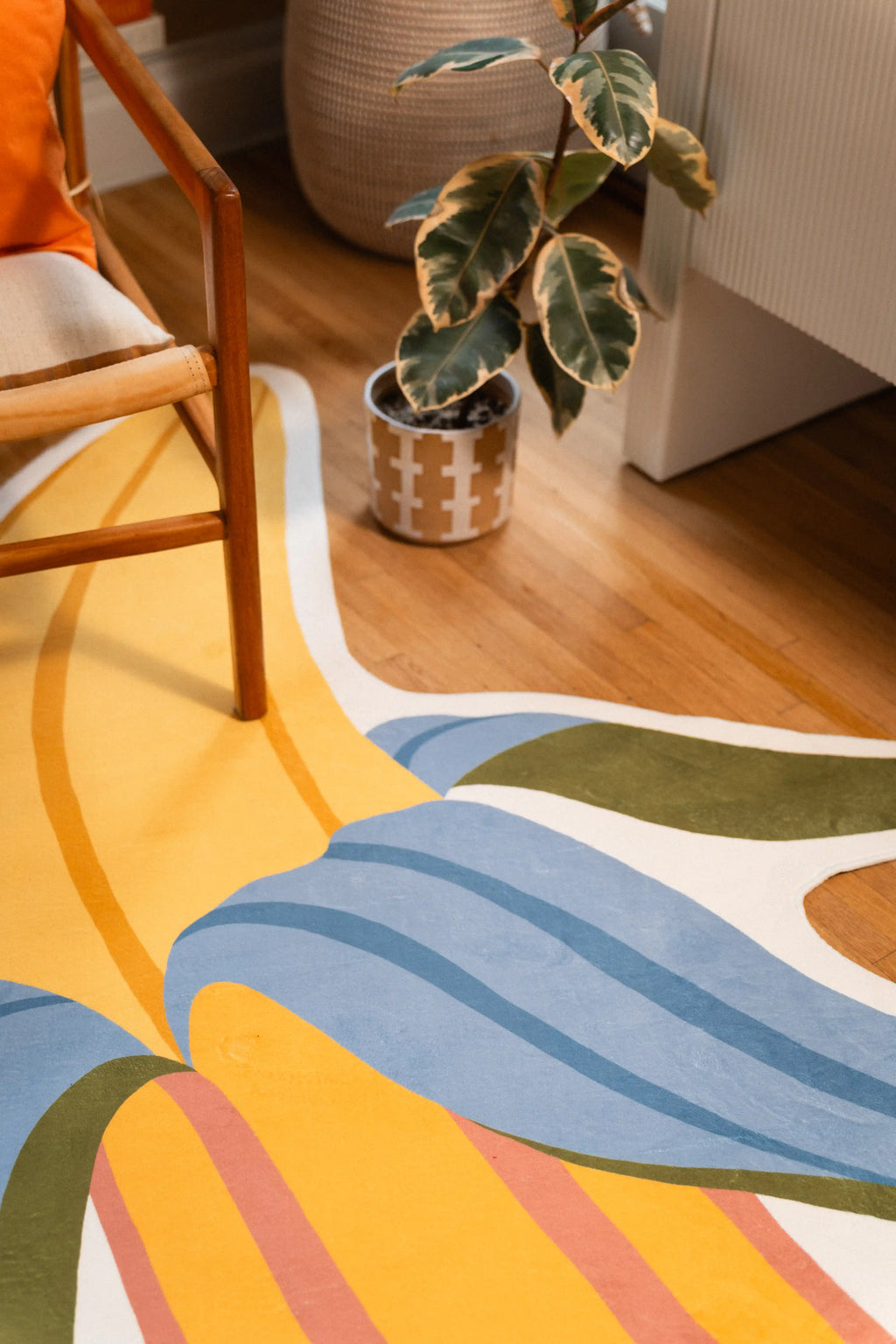 Blue striped peel and yellow banana fruit with a green peel tip beside a potted plant and white cabinet.