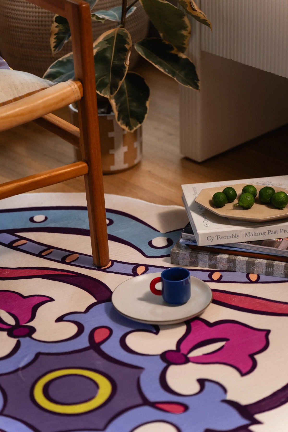 Floral area rug beneath a wooden chair leg with a blue cup and green fruit placed on the pattern.