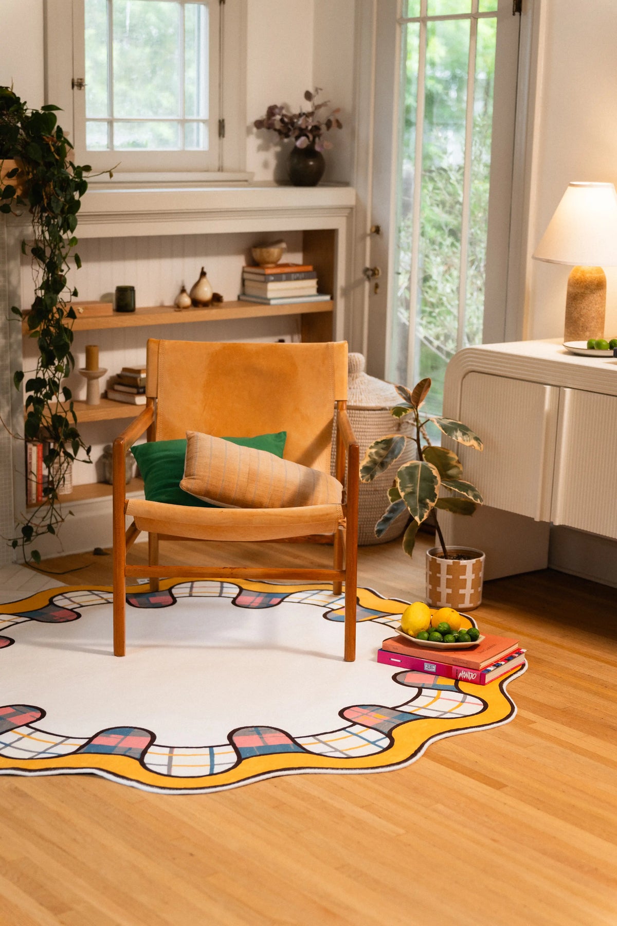 Round cream rug beneath a wooden armchair with a green cushion, framed by a yellow scalloped edge and plaid loops.