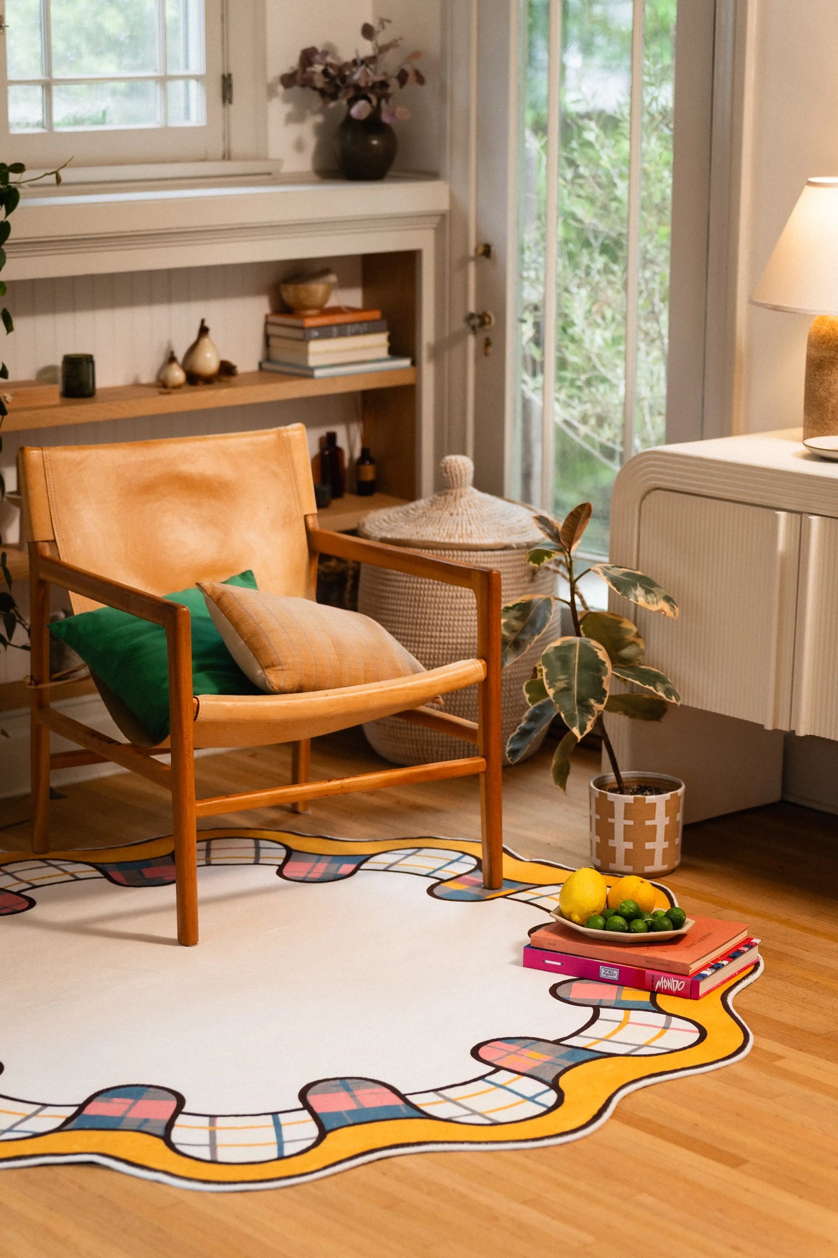 Cream-centered round rug beneath a wooden chair beside a potted plant and stacked books topped with fruit.