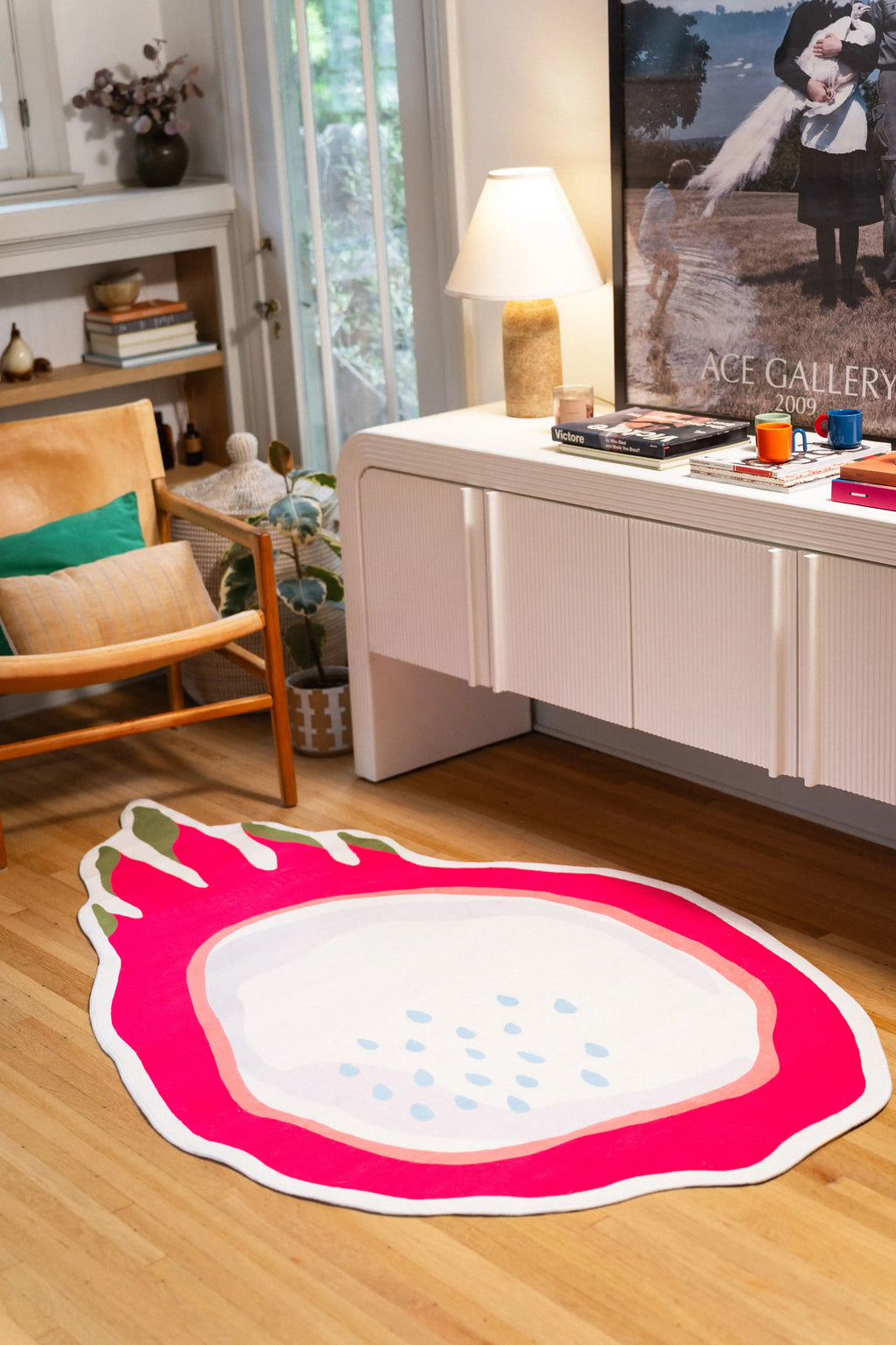 Dragon fruit-shaped rug with a hot pink rind, pale center, blue seeds, and green tips beside a wooden chair and white cabinet.