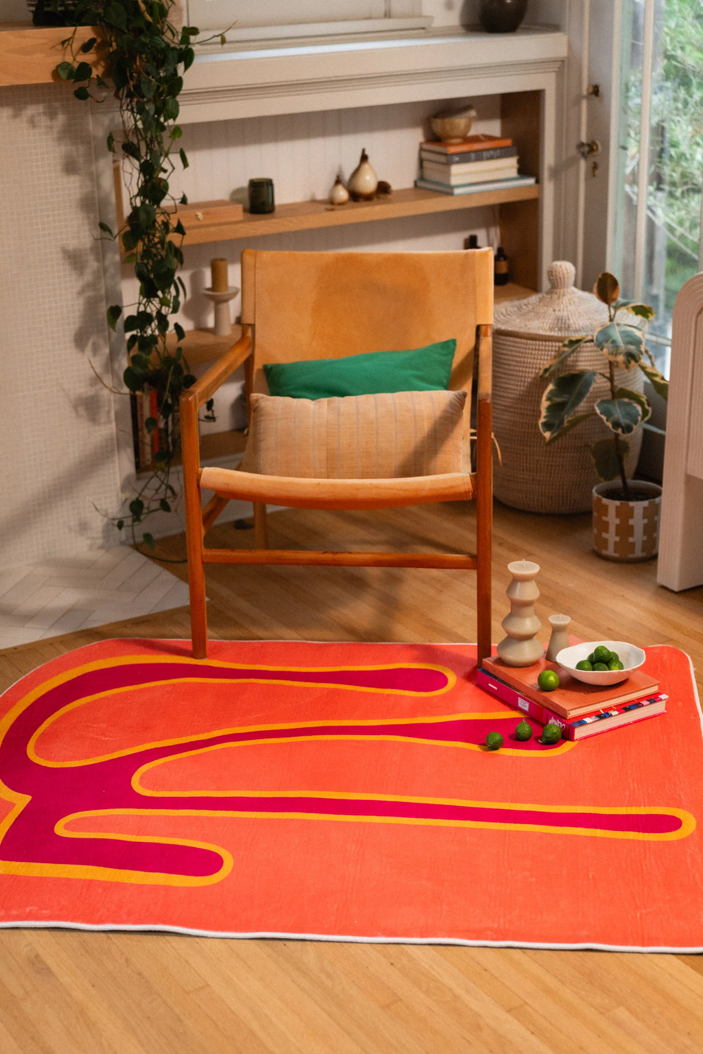 Angled view of a coral abstract rug beside a wooden chair, potted plants, and built-in shelves.
