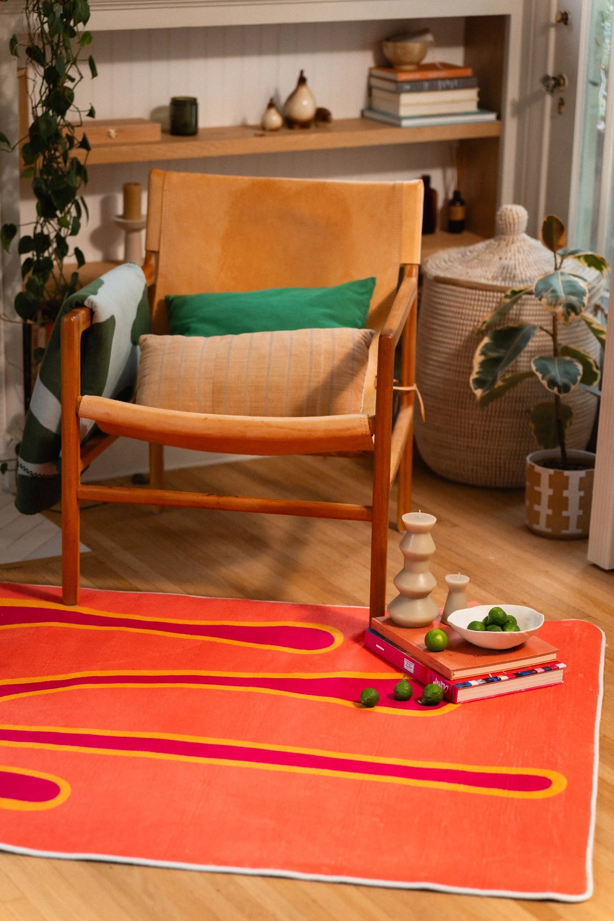 Coral orange rug with pooling magenta lines in front of a wooden chair with a green cushion.