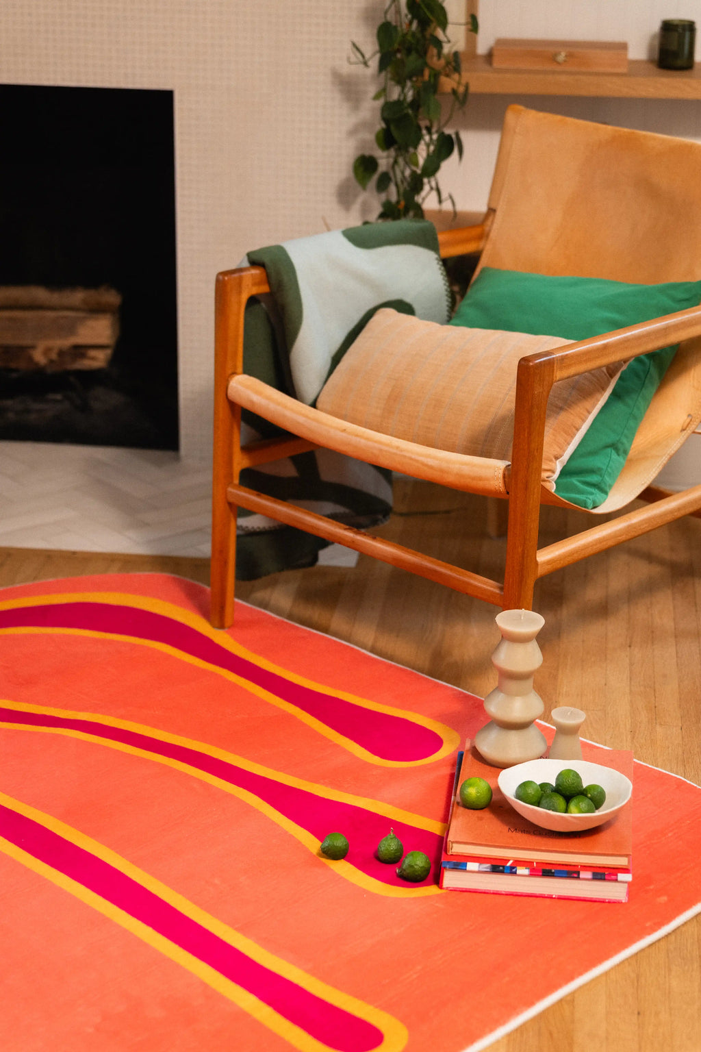 Close-up of an orange graphic rug with stacked books, a sculptural candle, and a bowl of green fruit.