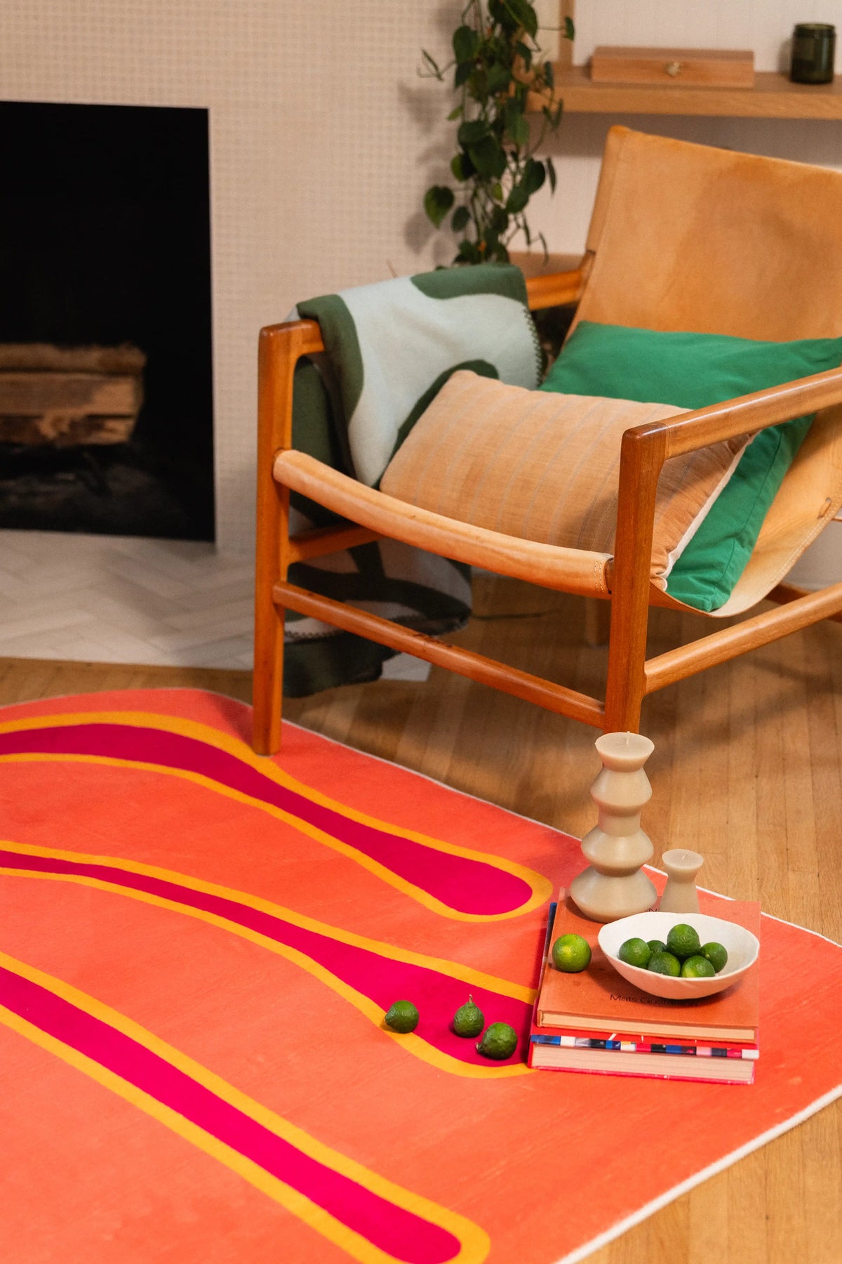 Close-up of an orange graphic rug with stacked books, a sculptural candle, and a bowl of green fruit.