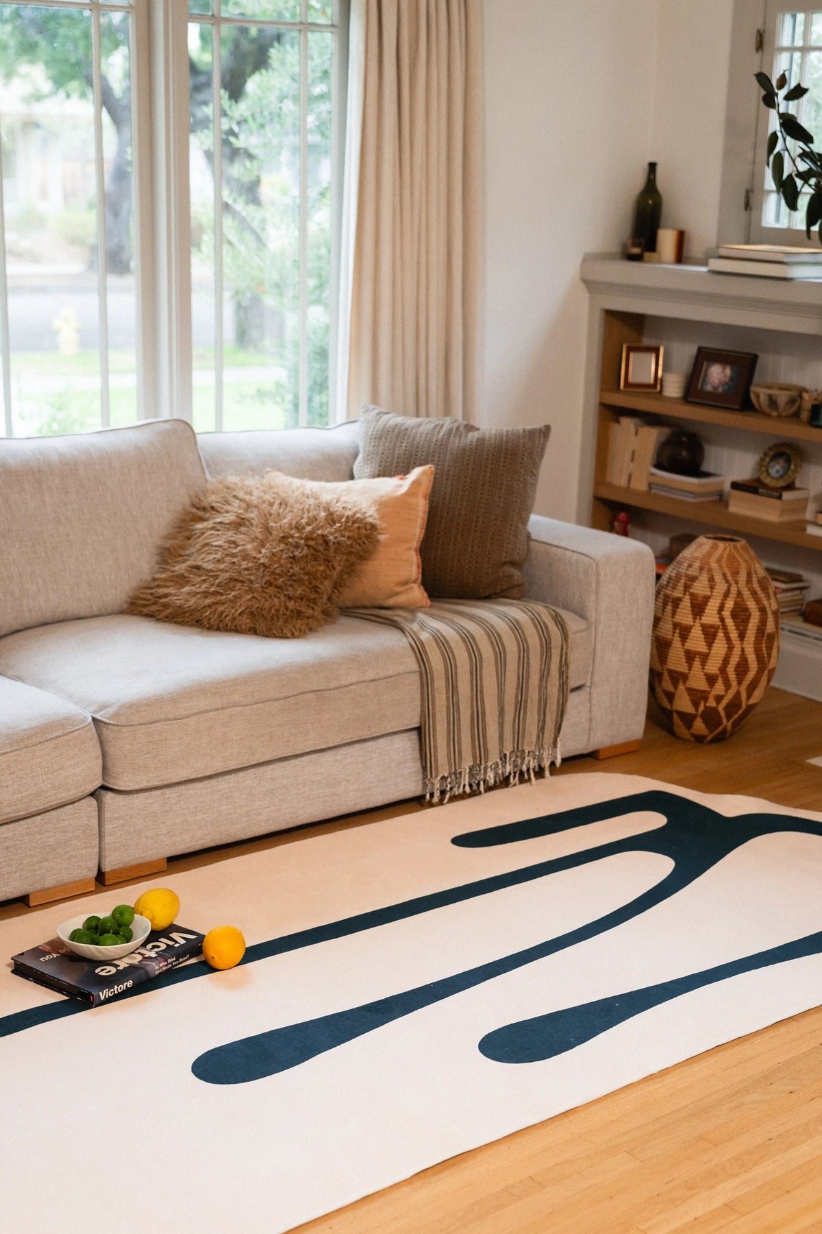 Beige abstract rug with deep green lines beside a gray sofa, with a small tray and fruit on top.