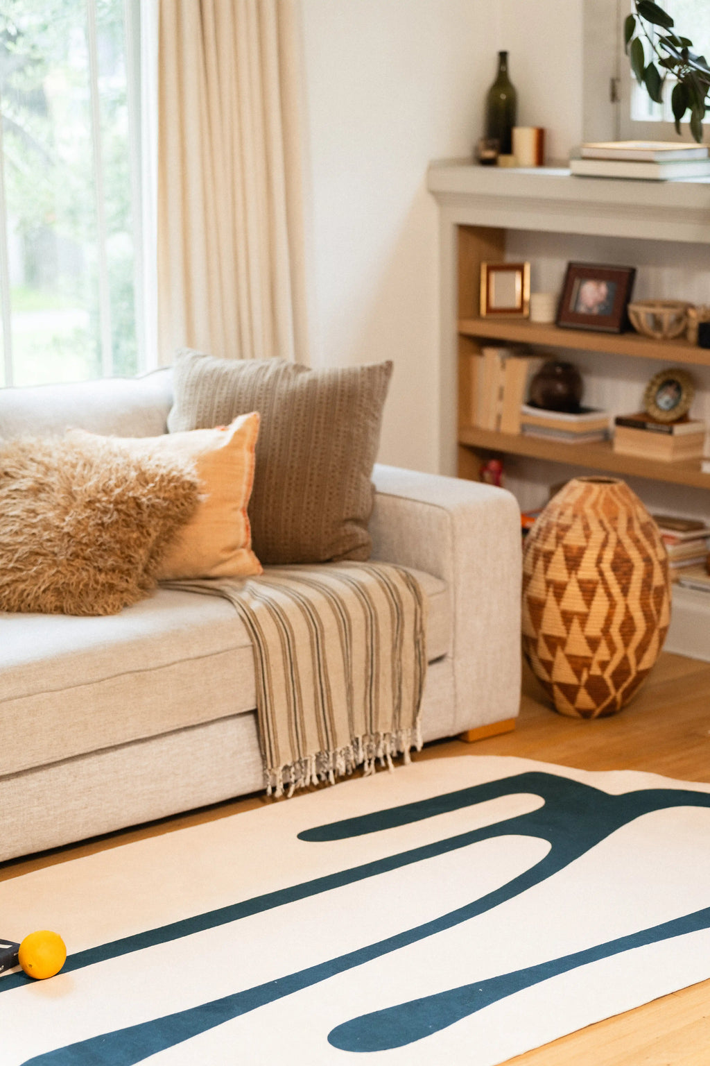 Beige rug with deep green melting lines beside a gray sofa and geometric wooden vase.