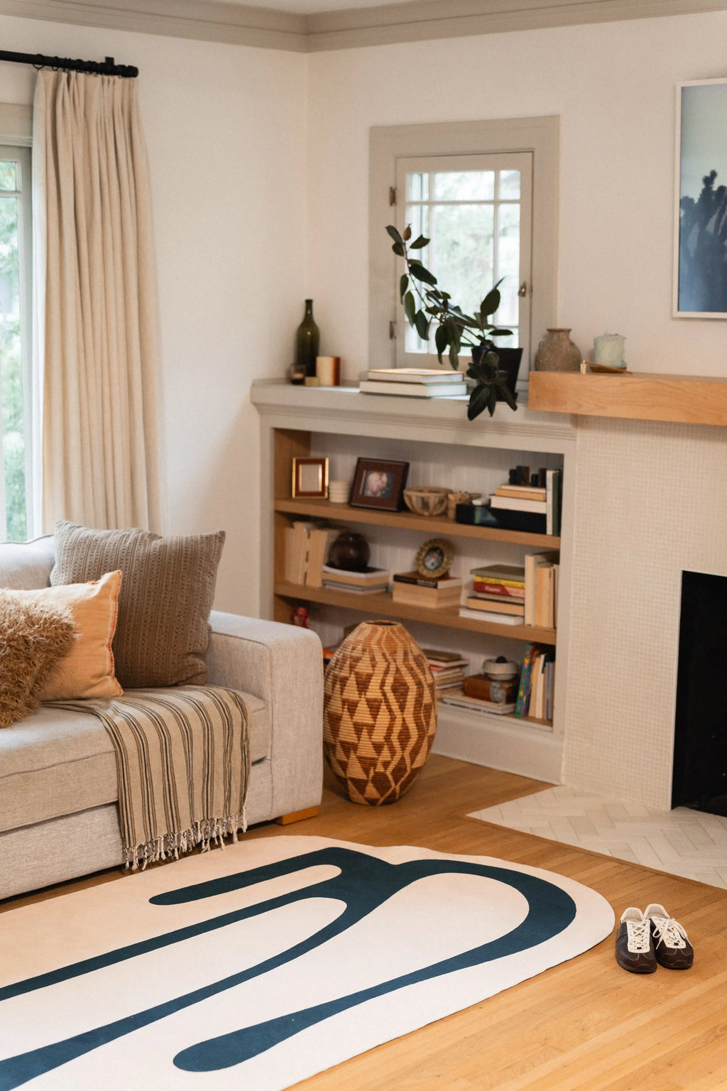 Long green drip shapes across a beige rug beside a gray sofa, built-in shelves, and fireplace.