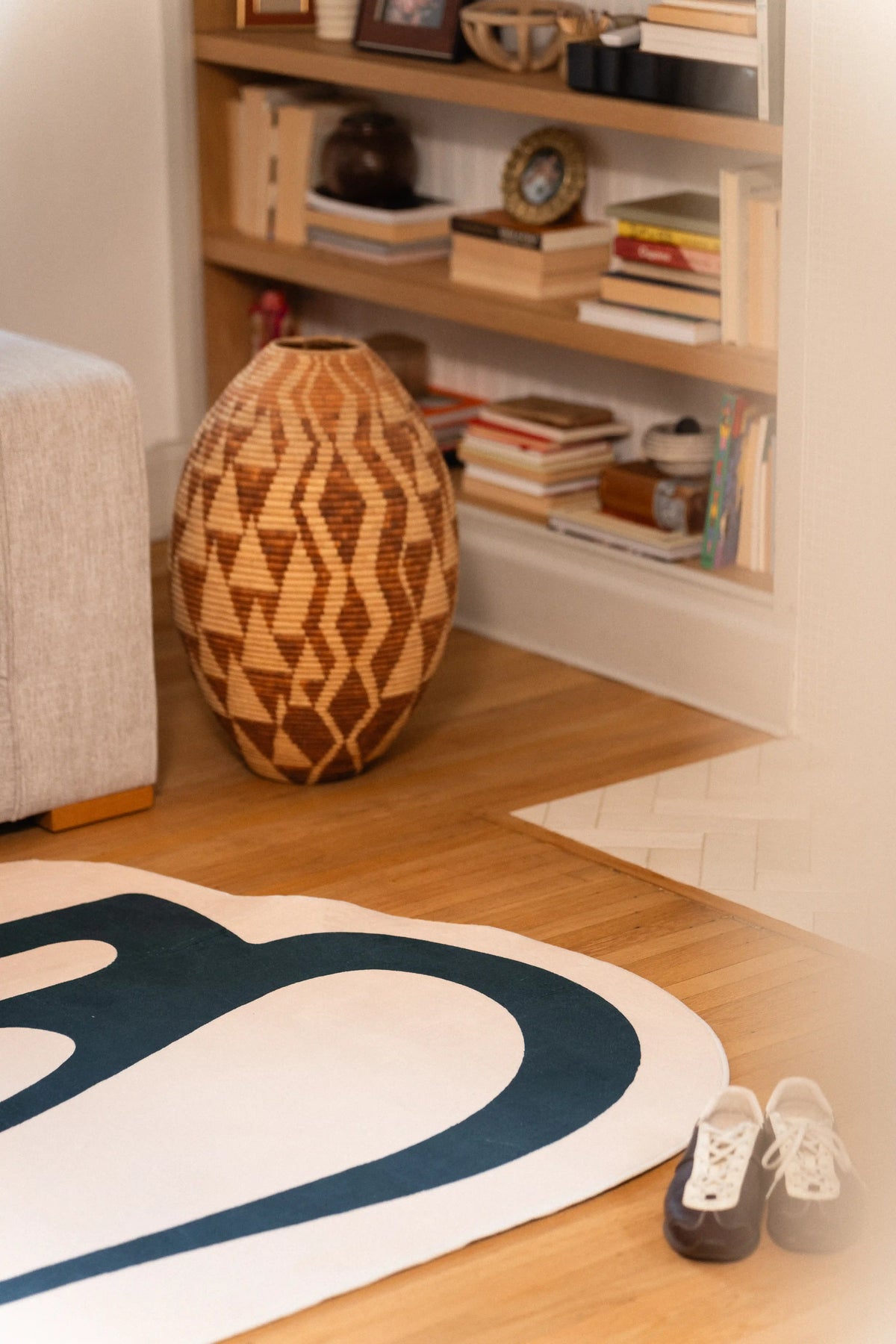 Corner of a beige abstract rug beside a geometric wooden vase and built-in living room shelves.