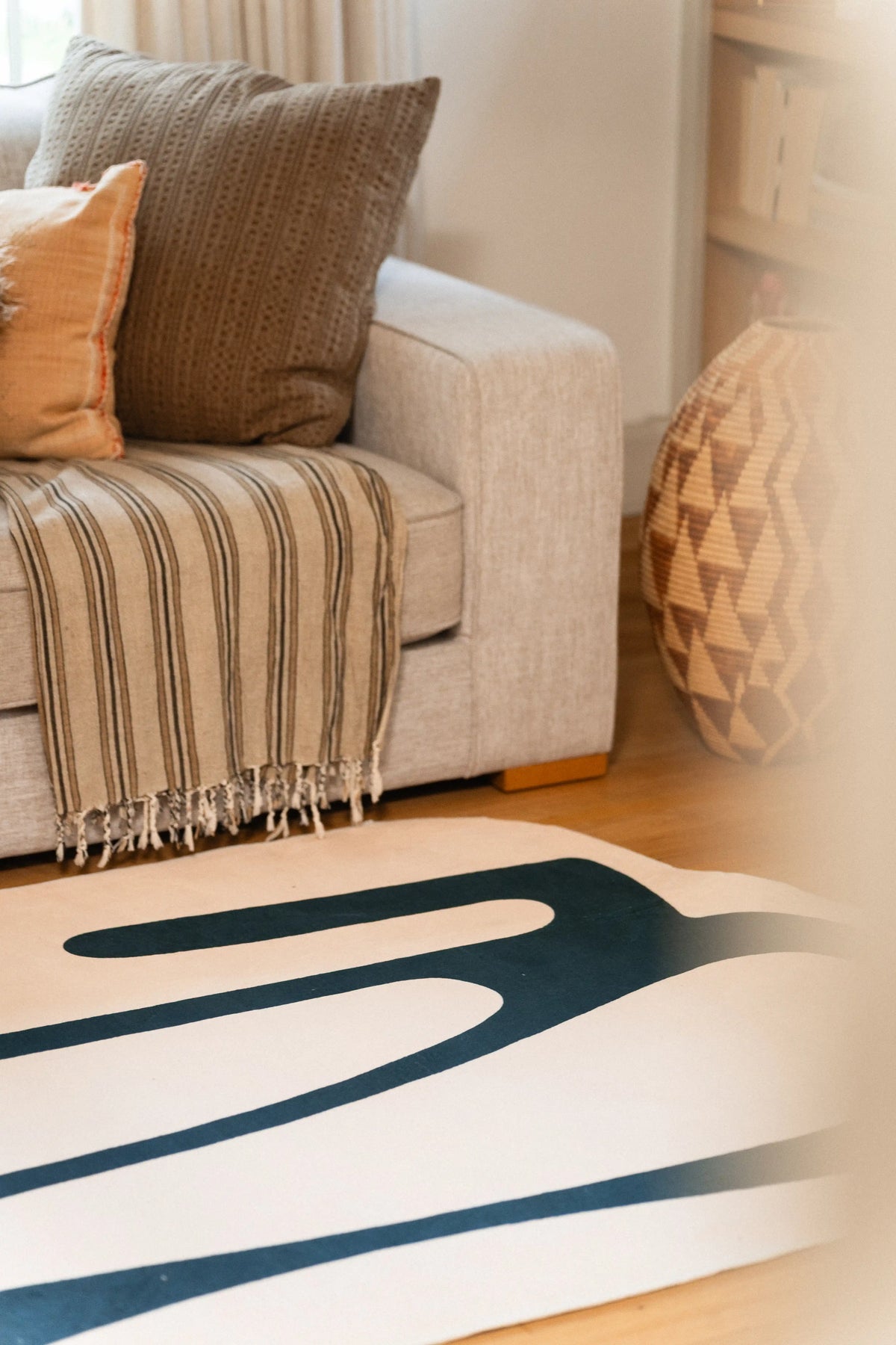 Rounded green lines on a beige rug beside a gray sofa, striped throw, and geometric wooden vase.