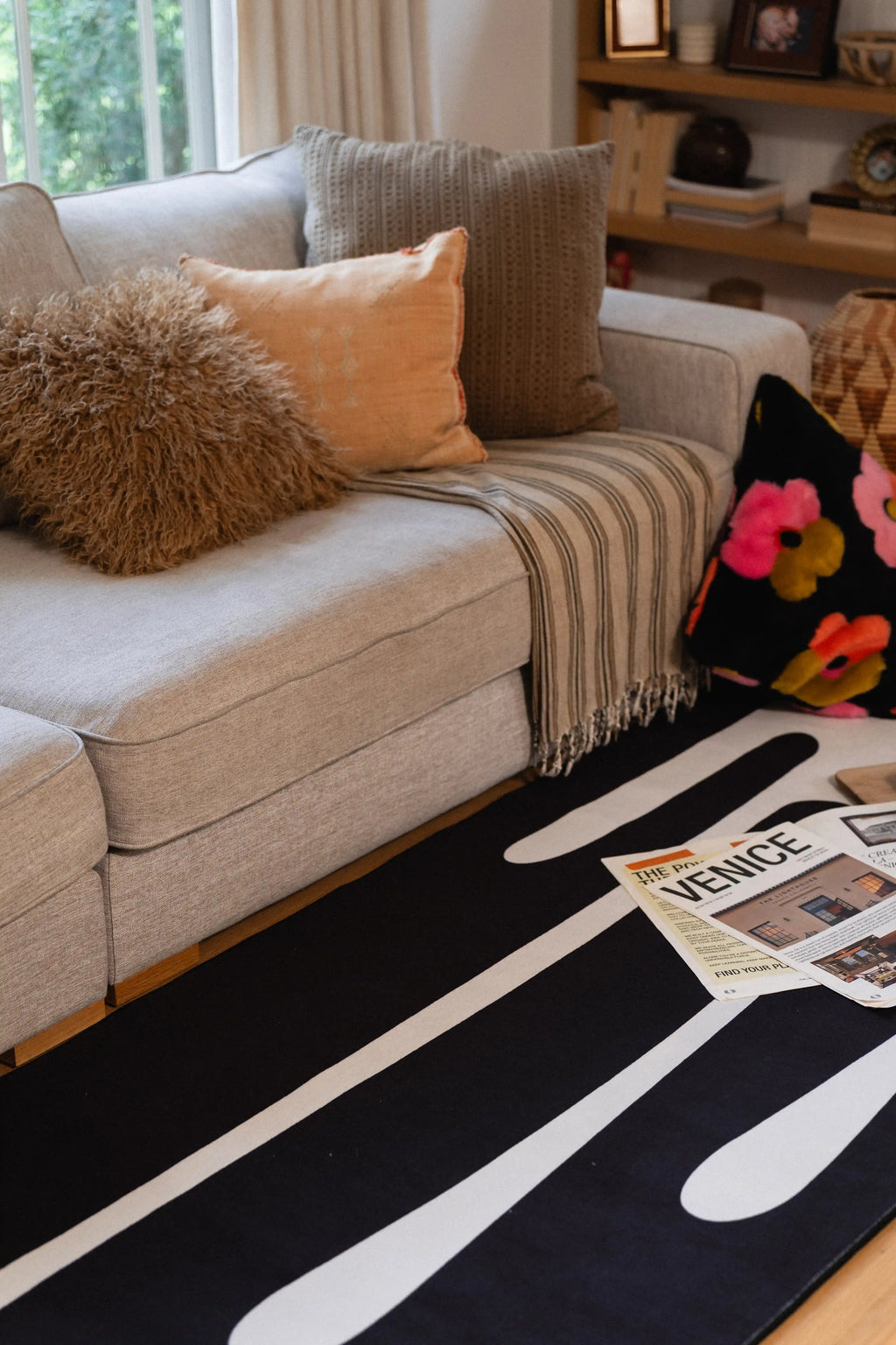 Black and white graphic rug running alongside a gray sofa with neutral pillows and a floral cushion.
