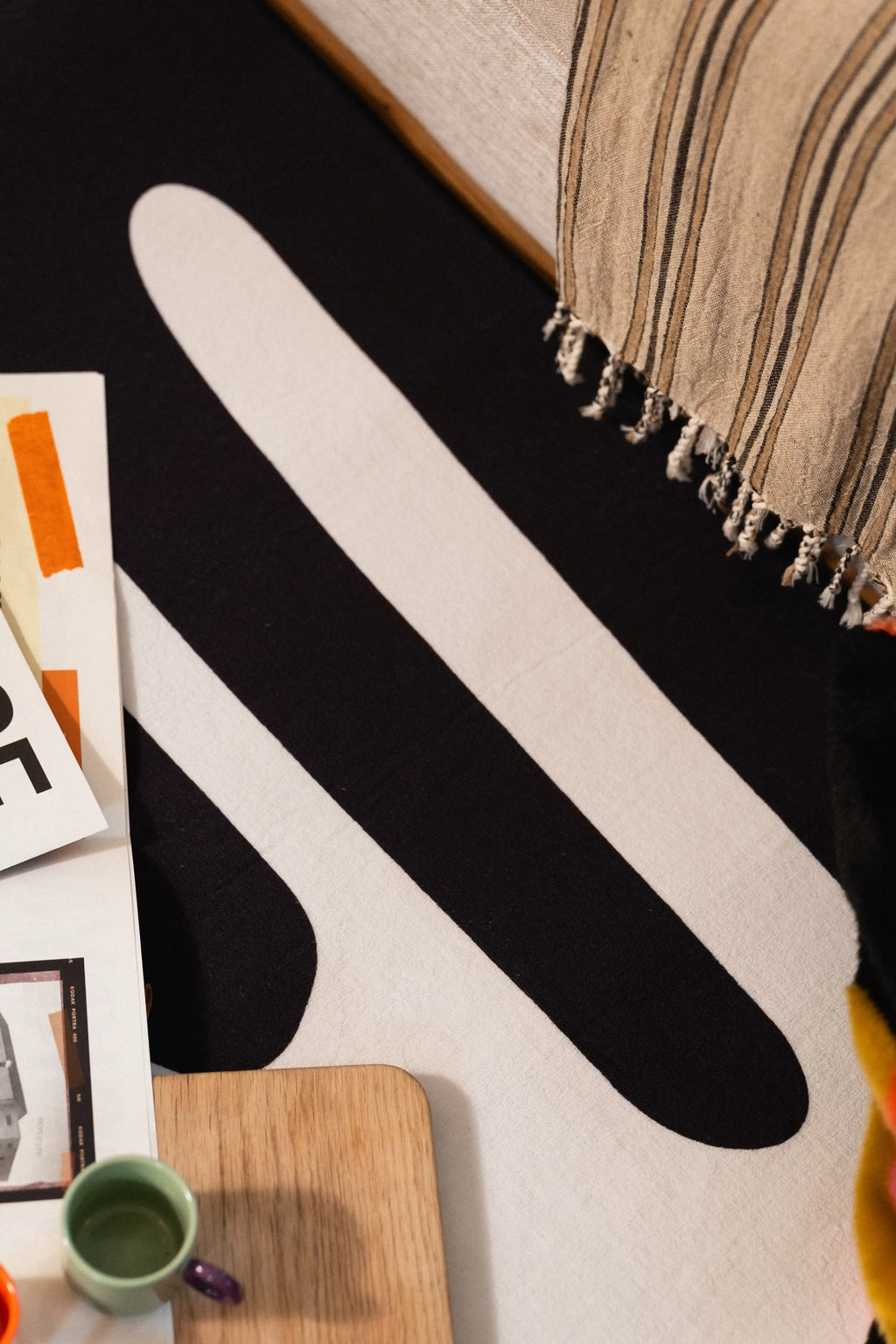 Close-up of long white lines across a black rug beneath the edge of a striped sofa throw.