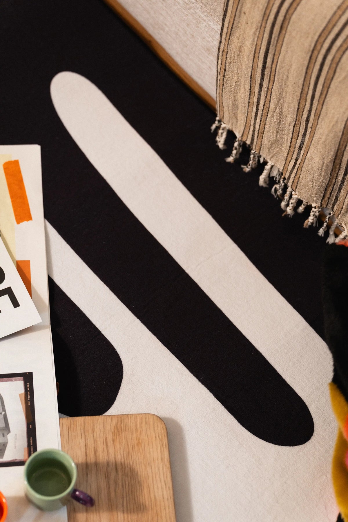 Close-up of long white lines across a black rug beneath the edge of a striped sofa throw.
