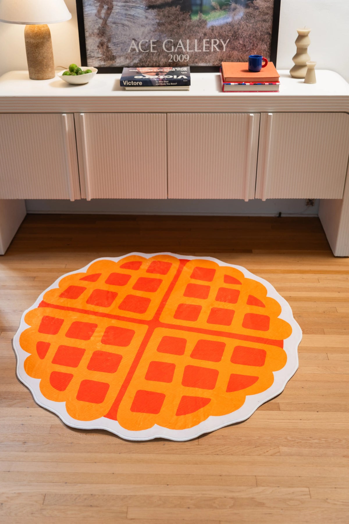 3' × 3' yellow and orange waffle rug centered on a wood floor in front of a white cabinet.