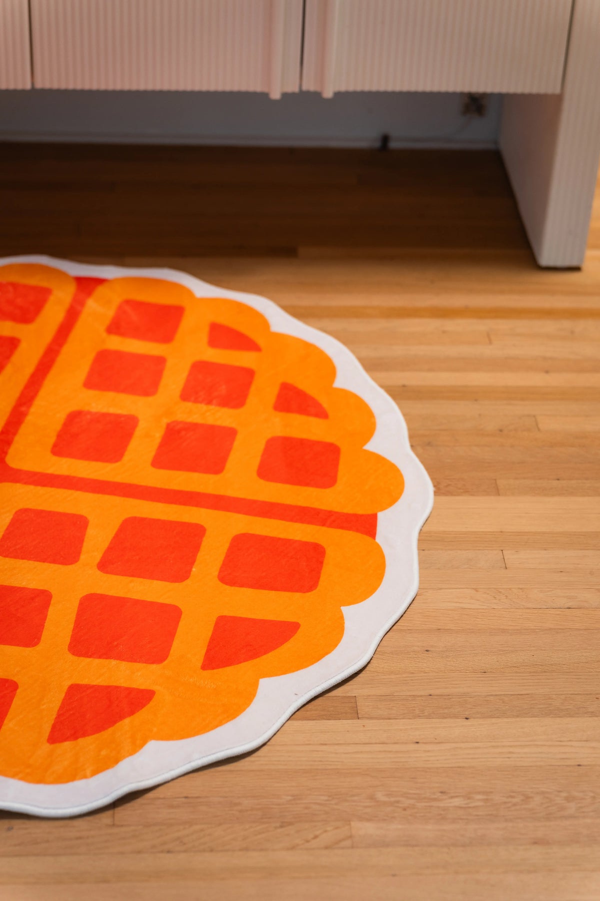 Partial yellow waffle rug with an orange grid and cream border in front of a white cabinet.