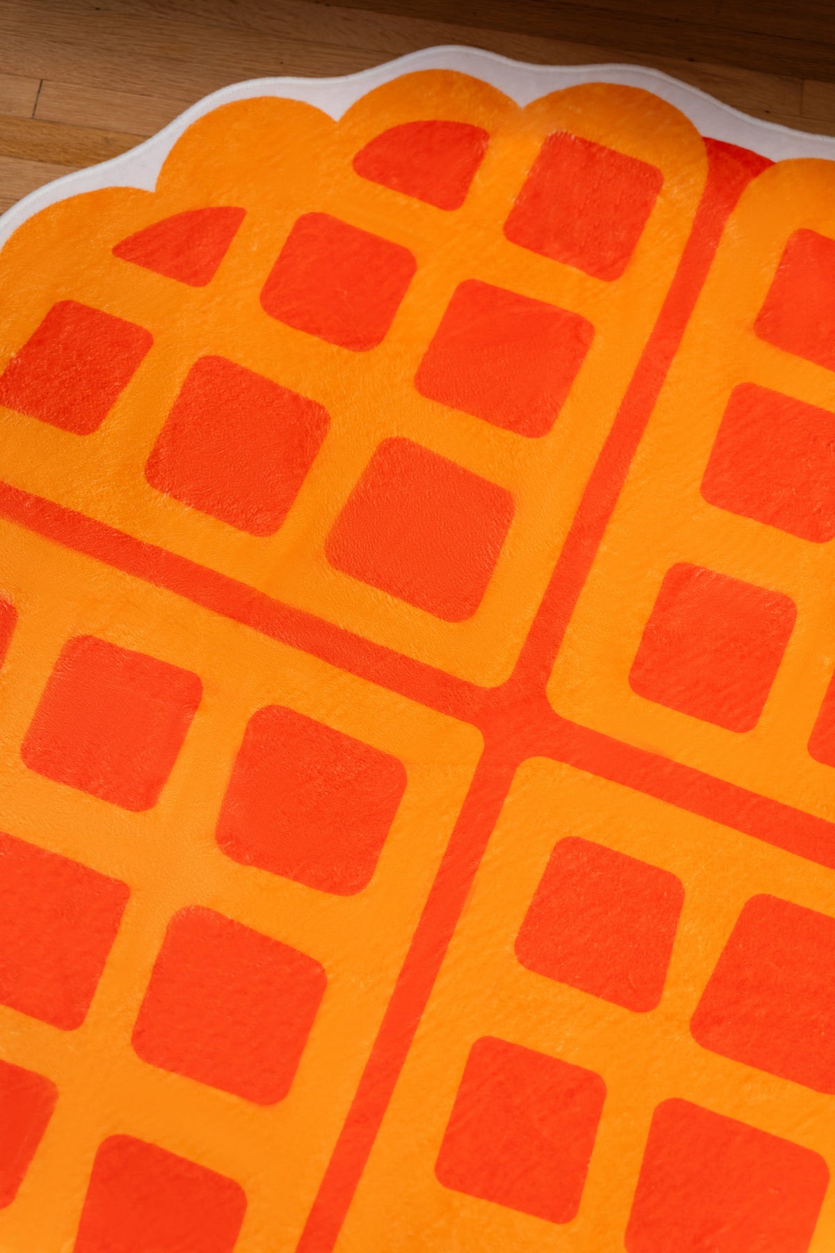 Orange waffle grid on a yellow rug with a rounded scalloped edge and cream outline.