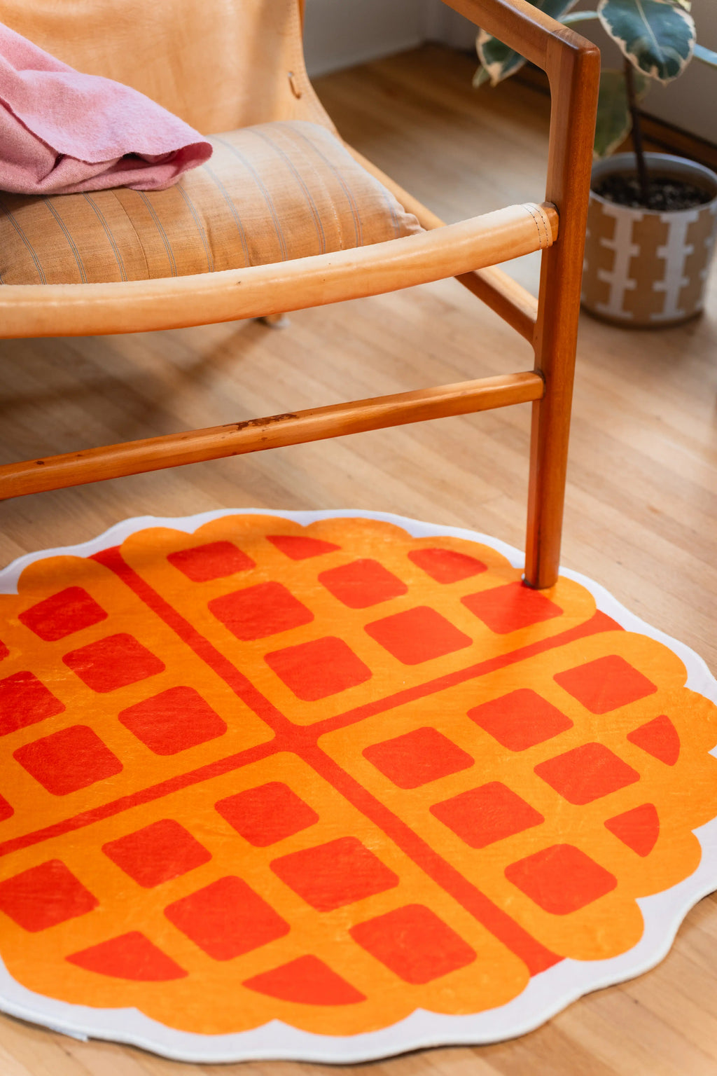Yellow waffle-shaped rug with orange square grids and a cream scalloped outline beneath a wooden chair.