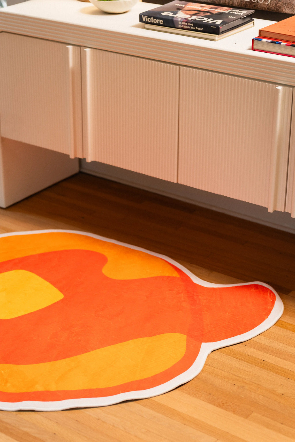 Orange syrup drip and yellow pancake edge on an irregular white-bordered rug beside a white cabinet.