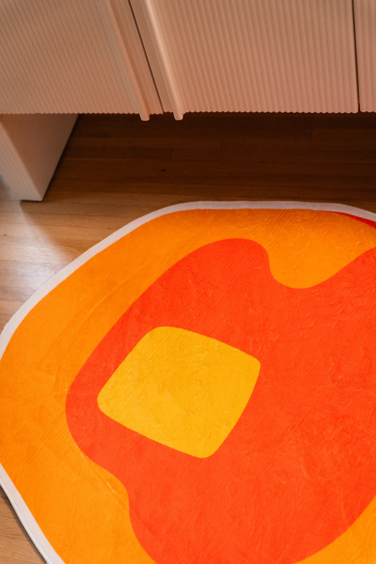 Yellow butter square on orange syrup at the center of a pancake-shaped rug beneath a white cabinet.