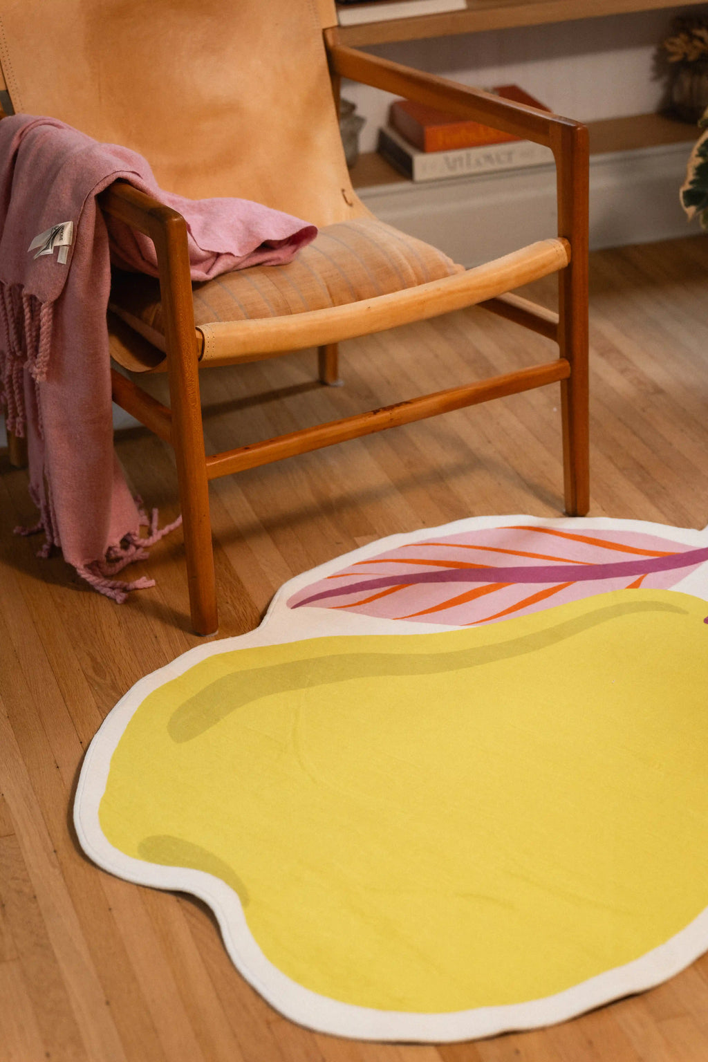 Yellow pear rug with a white outline and pink leaves in front of a wooden chair draped with a pink throw.