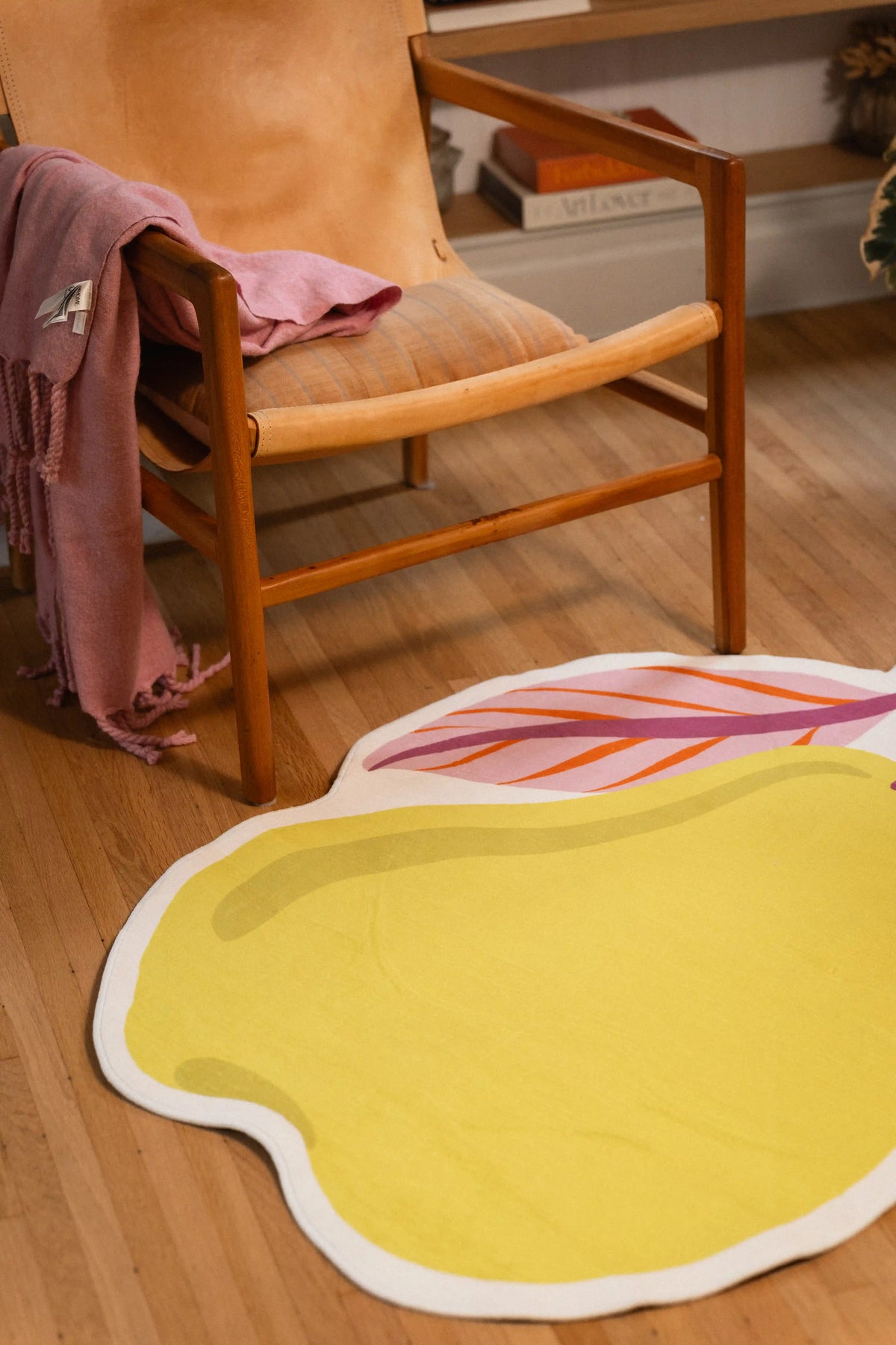 Yellow pear rug with a white outline and pink leaves in front of a wooden chair draped with a pink throw.