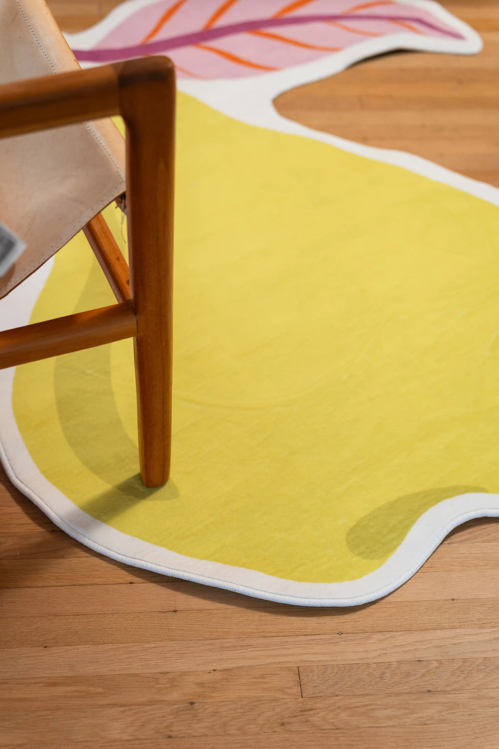 Yellow pear body with a white border beneath a wooden chair leg on a wood floor.