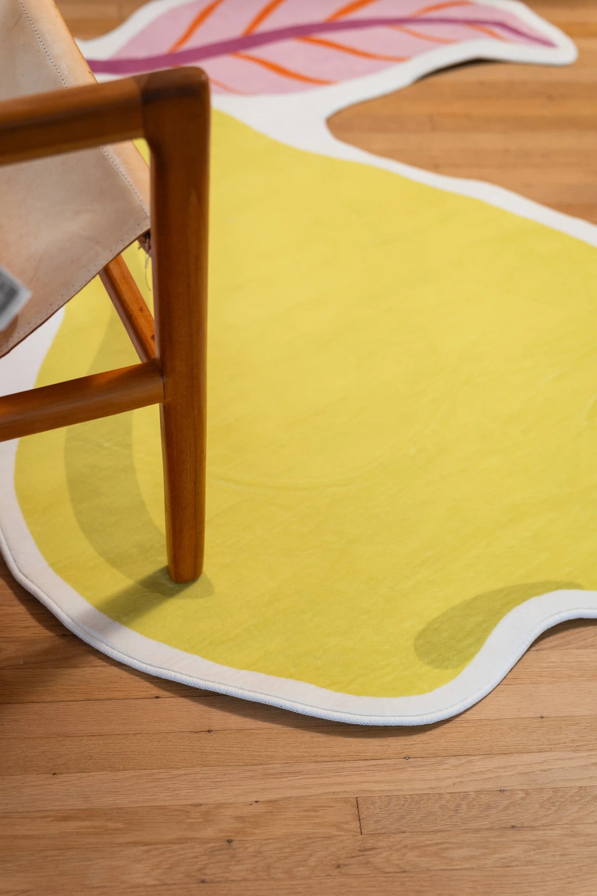 Yellow pear body with a white border beneath a wooden chair leg on a wood floor.